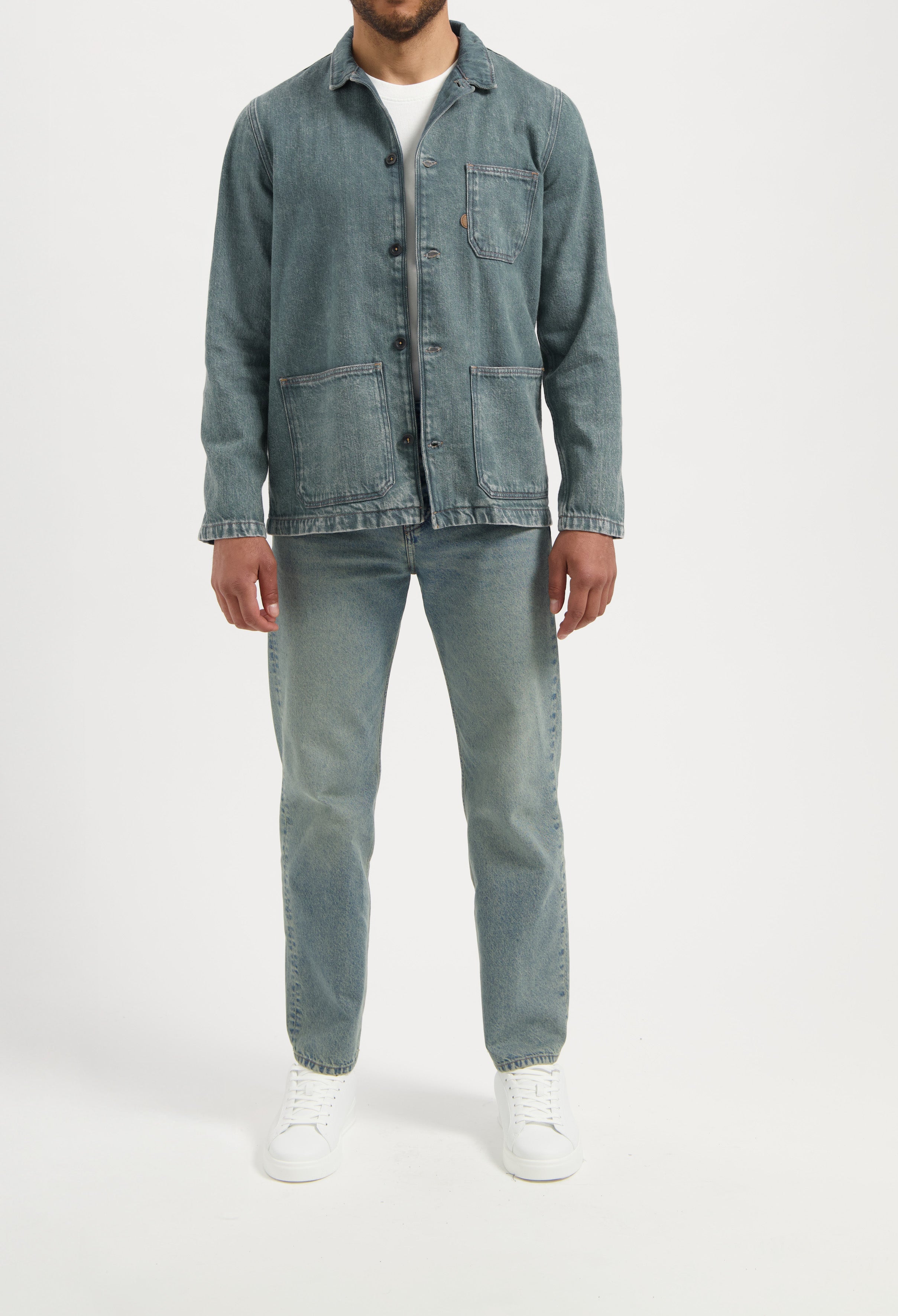 Sustainable MUD Jeans in light blue denim, ethically crafted, worn with a white T-shirt and white sneakers.