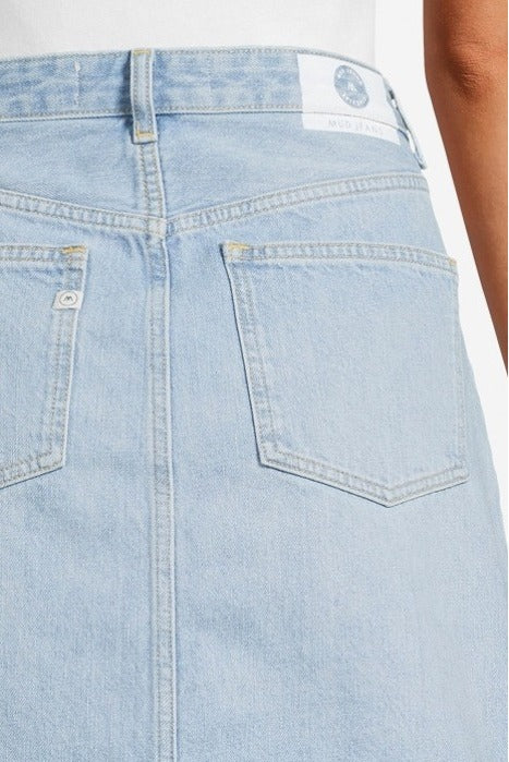 Light blue denim skirt made from organic cotton, featuring rear pockets and visible stitching, worn with a white top.