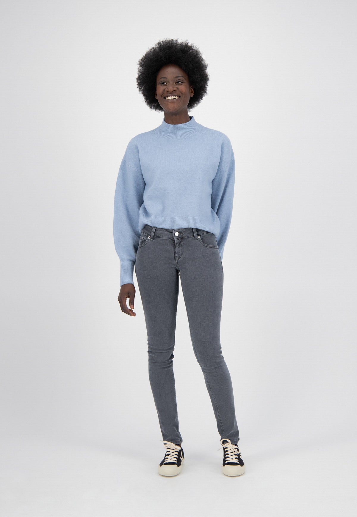 Person wearing a light blue sweater with puffed sleeves and fitted gray jeans, paired with black and white sneakers.