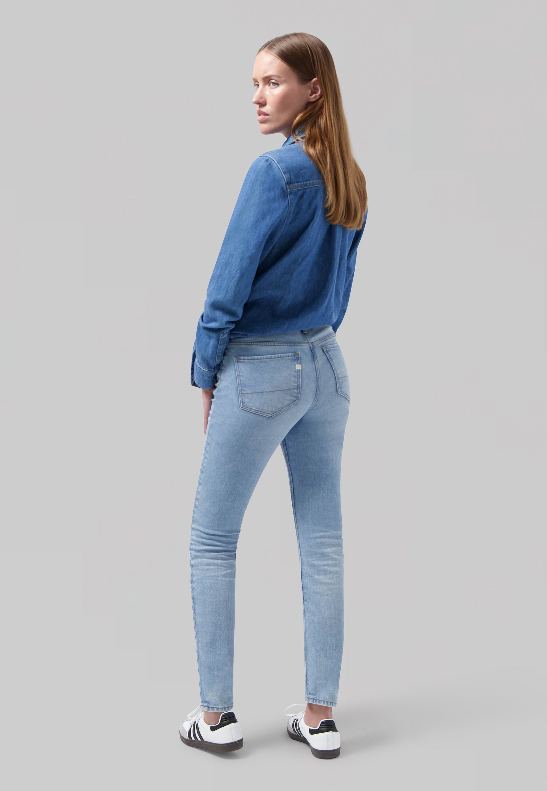 Mid-length denim shirt and light blue skinny jeans, styled with white and black sneakers, showcasing casual fashion ensemble.