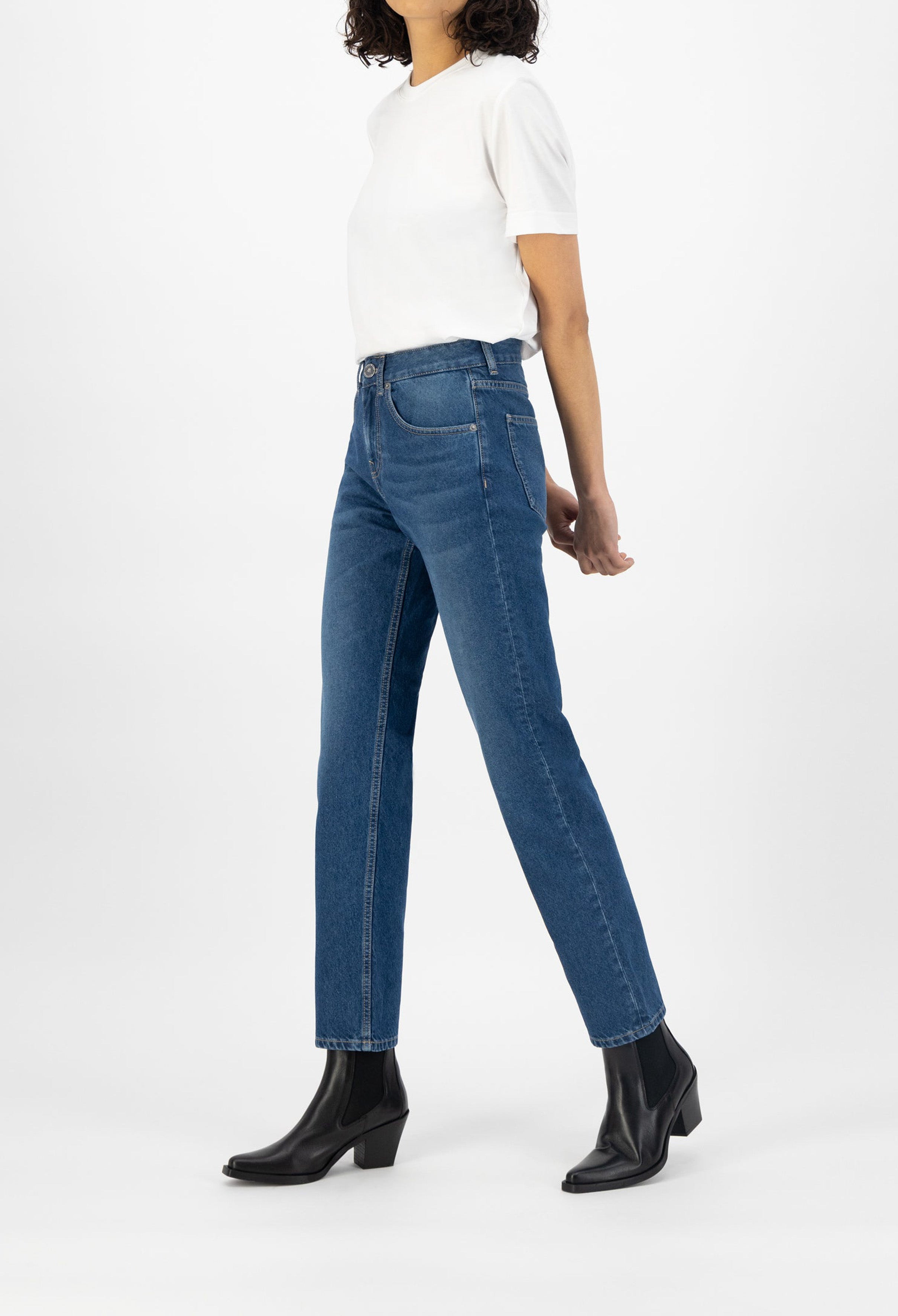 Woman wearing casual blue straight-leg jeans and a white short-sleeve top, paired with black leather ankle boots.