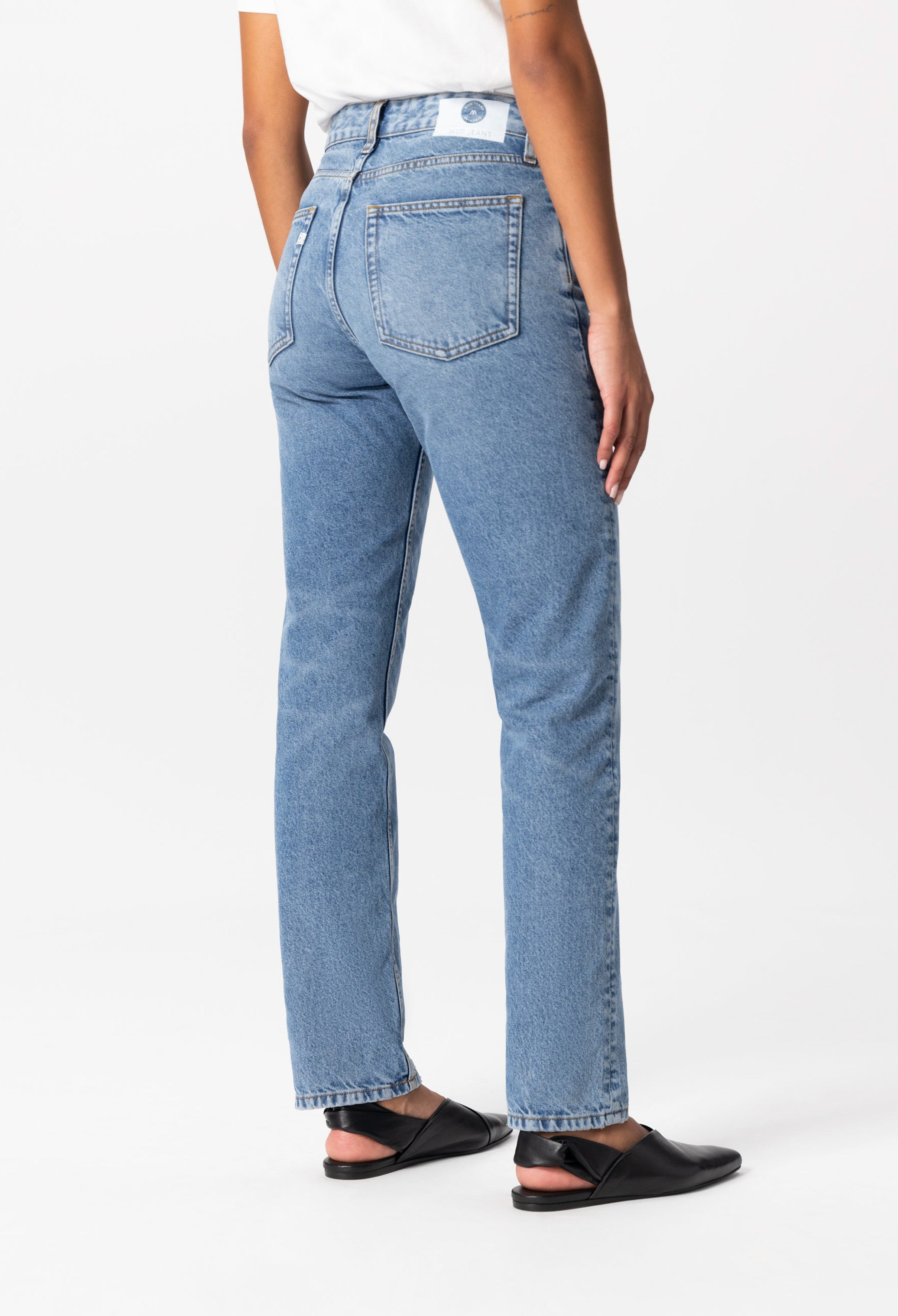 High-waisted light blue denim jeans with back patch pockets, worn by a person in black flats and a casual white shirt.