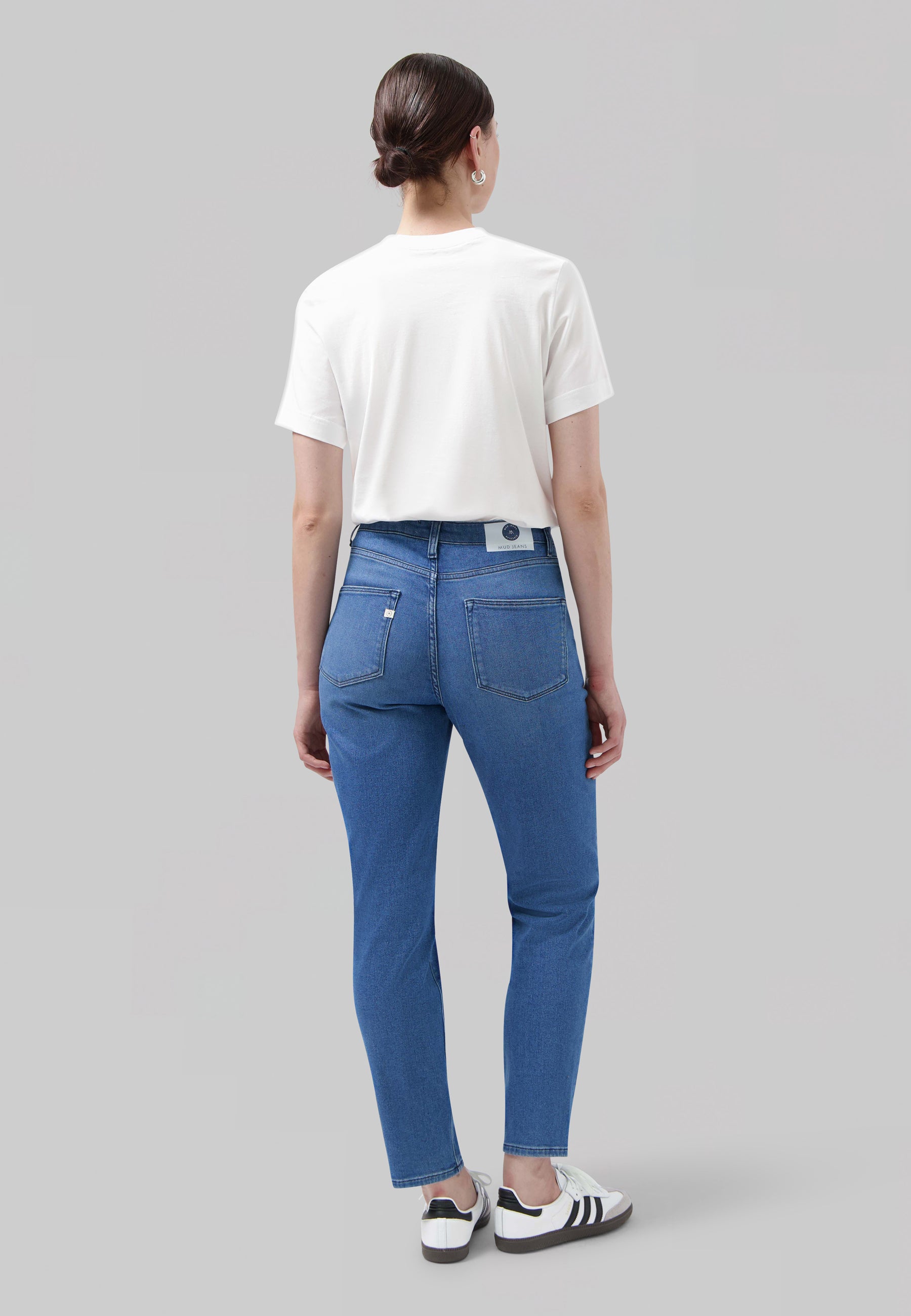 Casual white tee paired with mid-blue jeans, highlighting a comfortable fit and back pocket details, worn with sports sneakers.