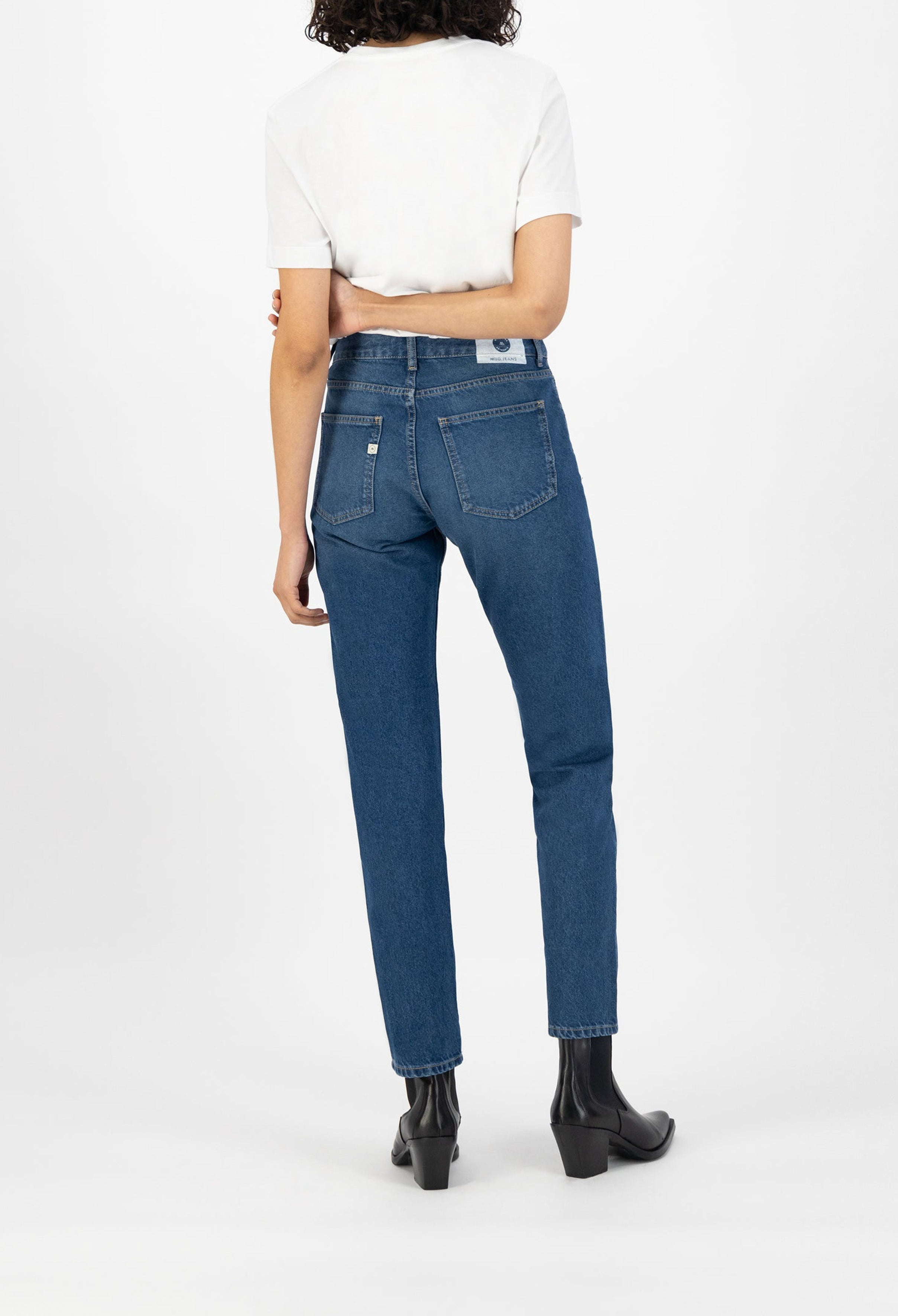 Straight-leg blue MUD Jeans made from organic cotton, shown on a person wearing a white T-shirt and black heeled boots.
