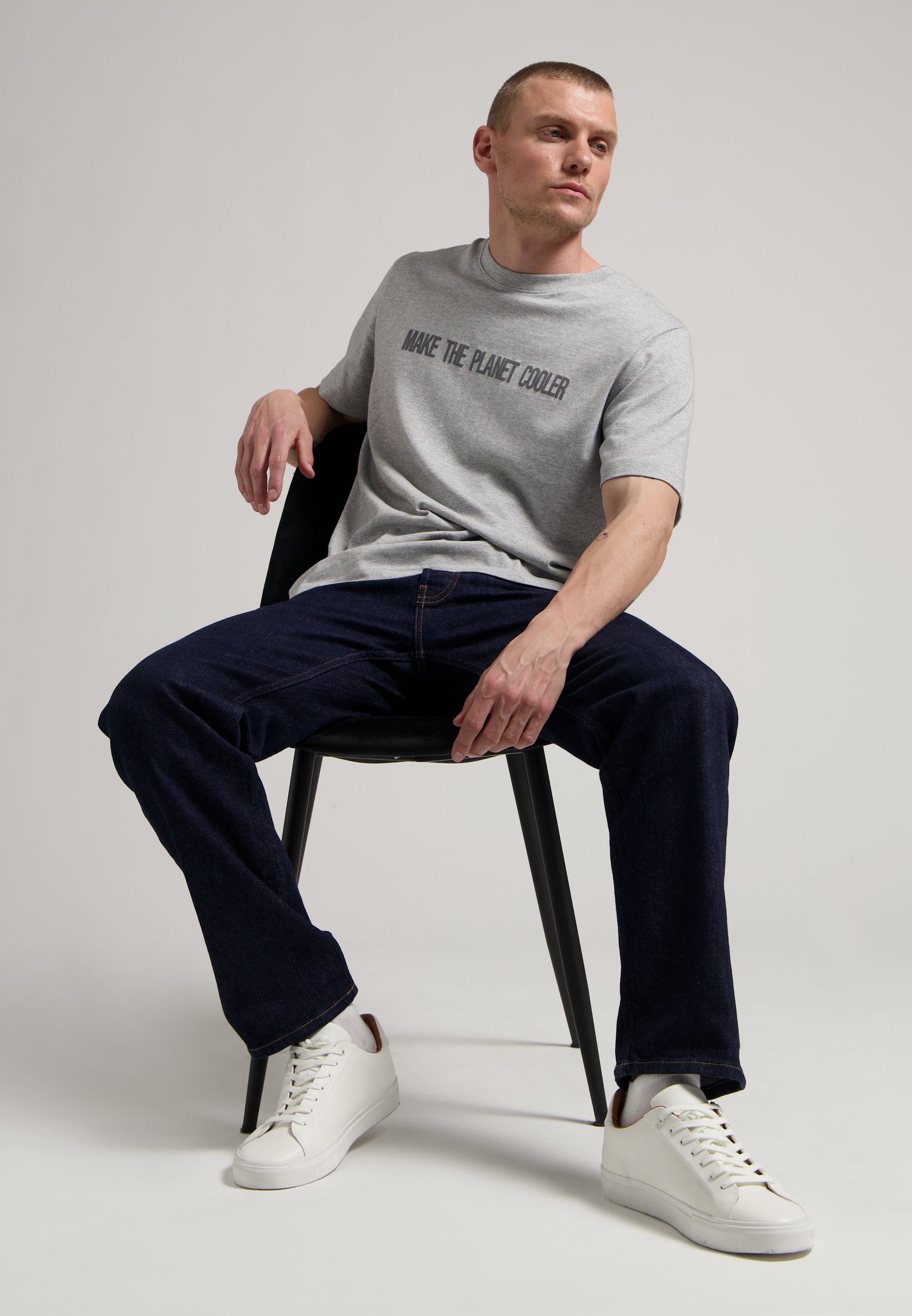 Sustainable MUD Jeans in blue denim, paired with a black t-shirt featuring an eco-friendly slogan and white sneakers.