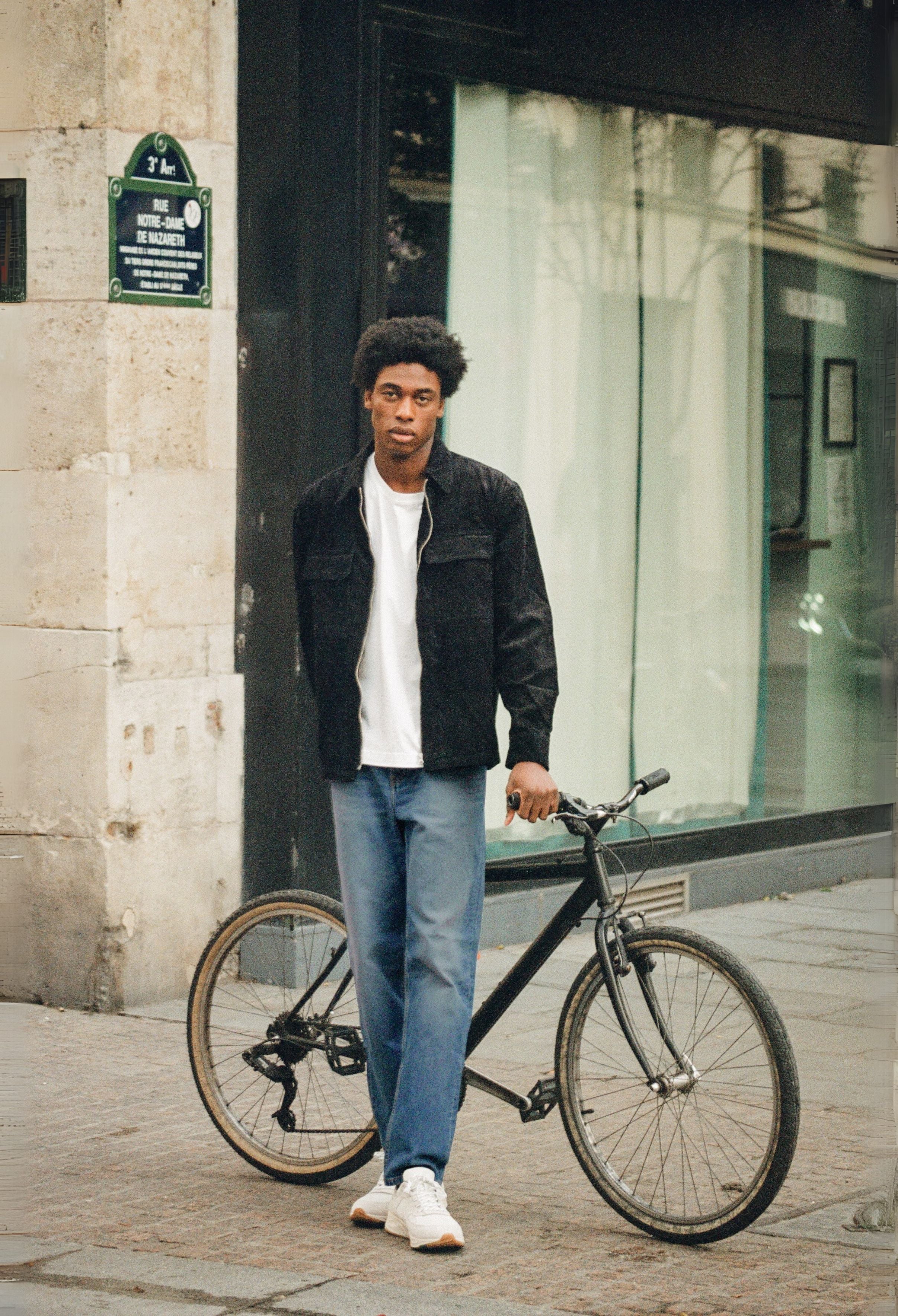 Sustainable MUD Jeans in deep blue denim, crafted from organic cotton, worn with a gray sweater and white sneakers.