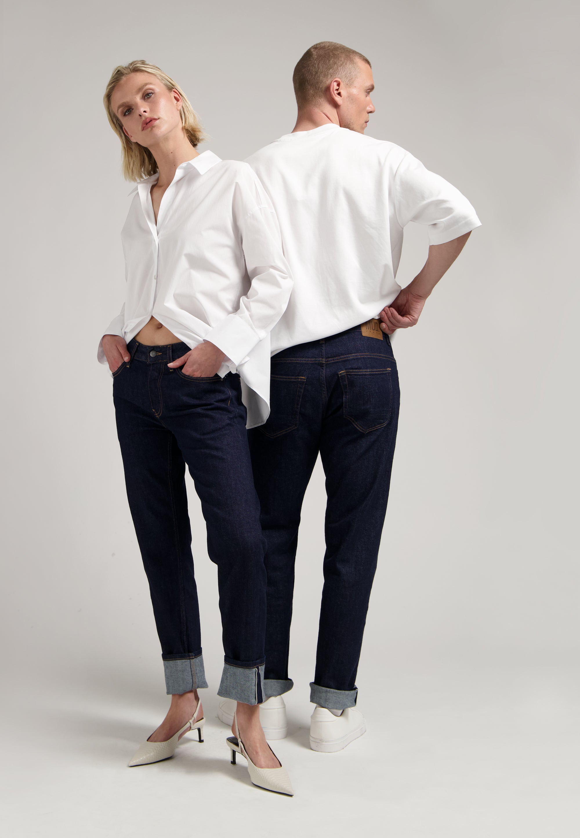 Sustainable MUD Jeans in a classic medium blue wash, crafted ethically from organic cotton, worn with a gray sweater.