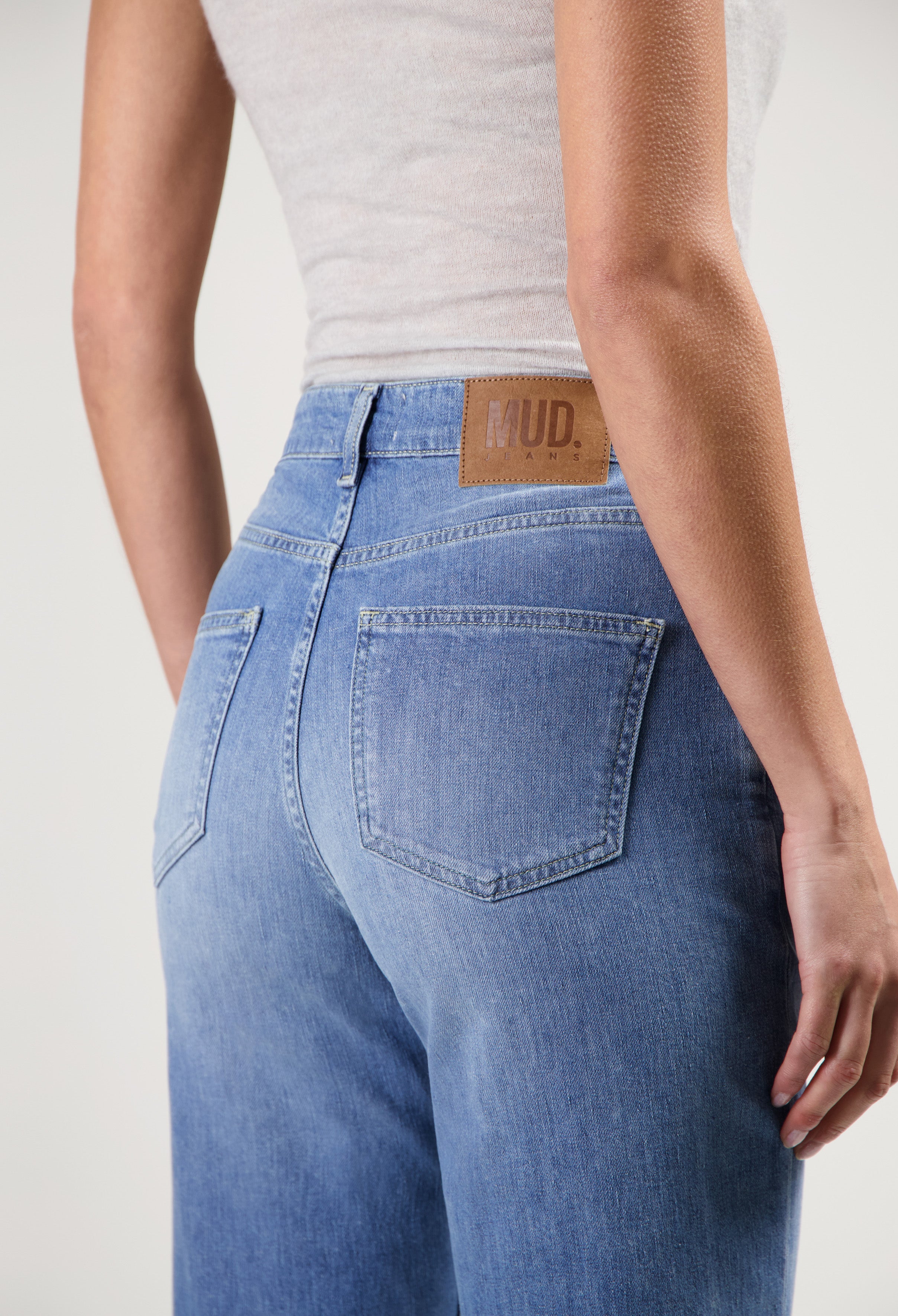 Back view of MUD Jeans made from sustainable materials, showing high-waisted, light blue denim worn with a white top.