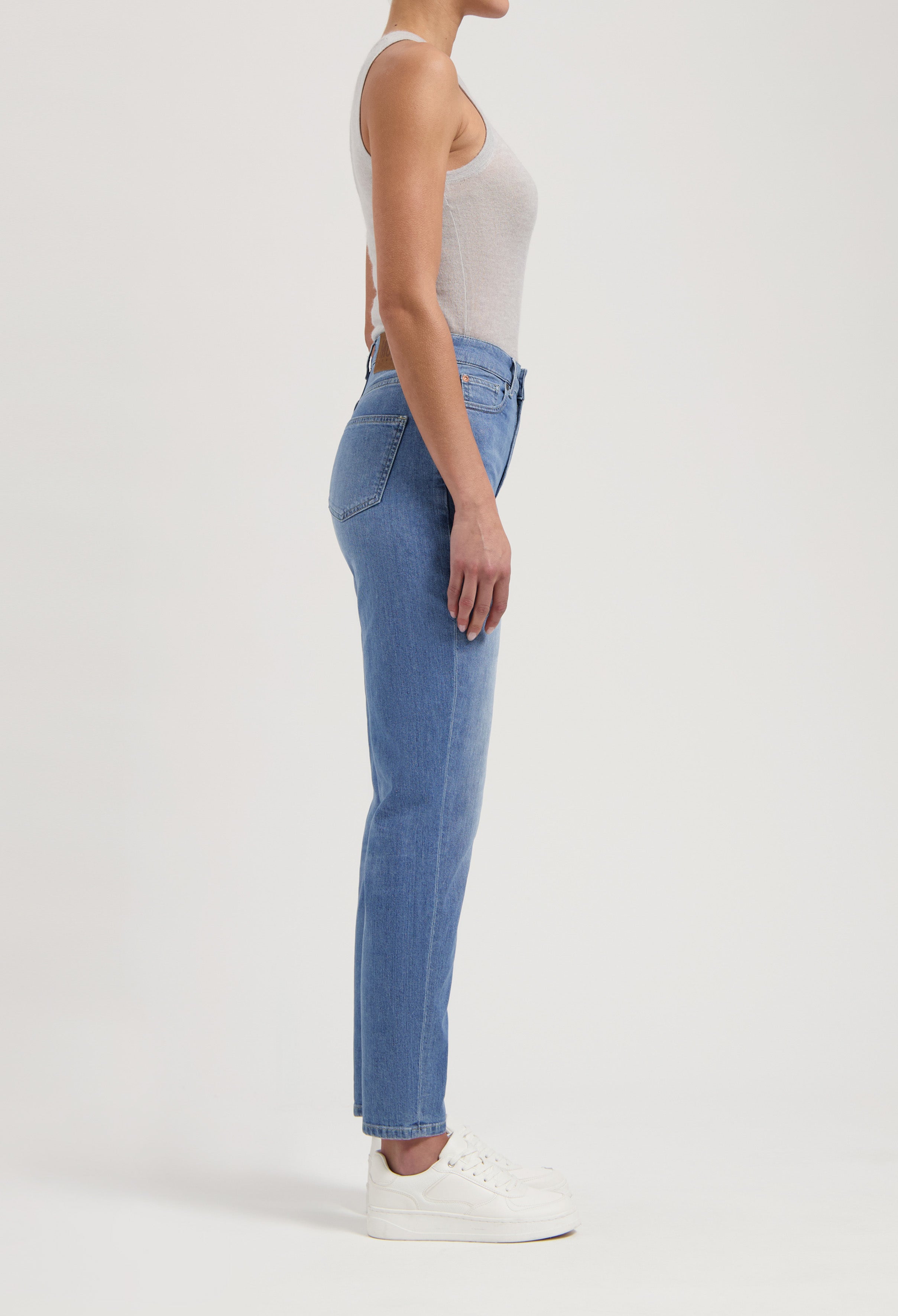 Woman wearing light blue slim-fit jeans paired with a gray sleeveless top, shown in a side profile against a plain background.