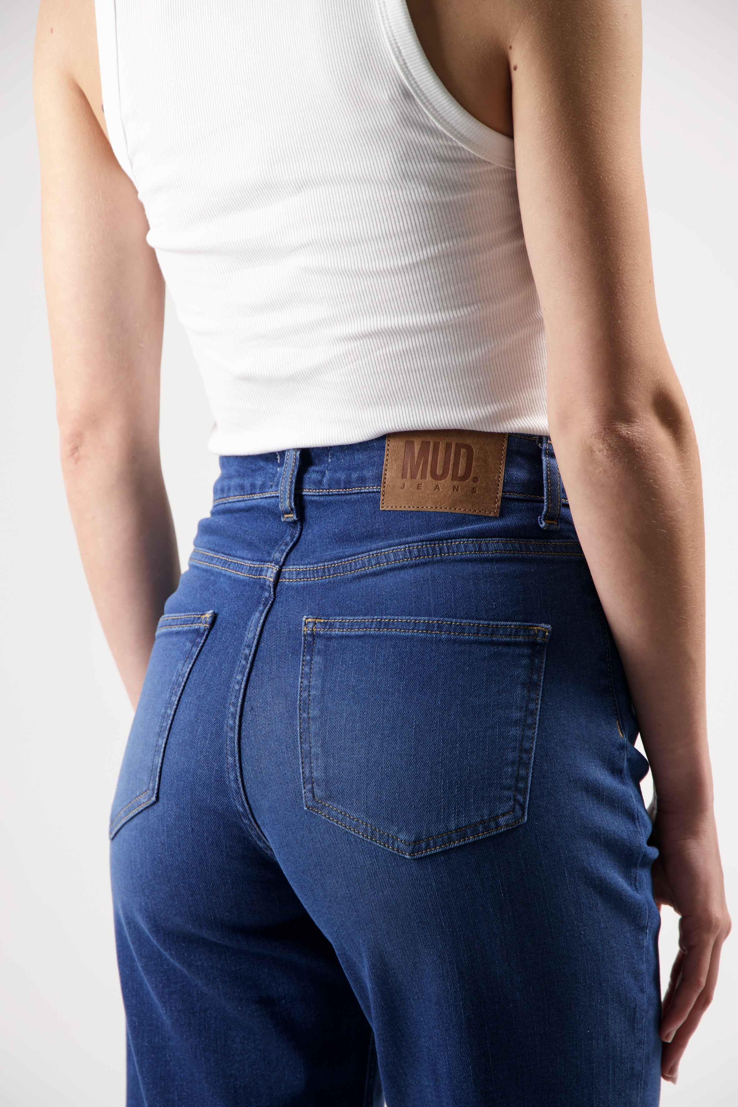 Person wearing sustainable MUD Jeans made of organic cotton with a white ribbed tank top, showcasing the denim's back details.