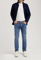 Sustainable MUD Jeans in light blue denim, crafted from organic cotton, paired with a white sweater for a classic look.