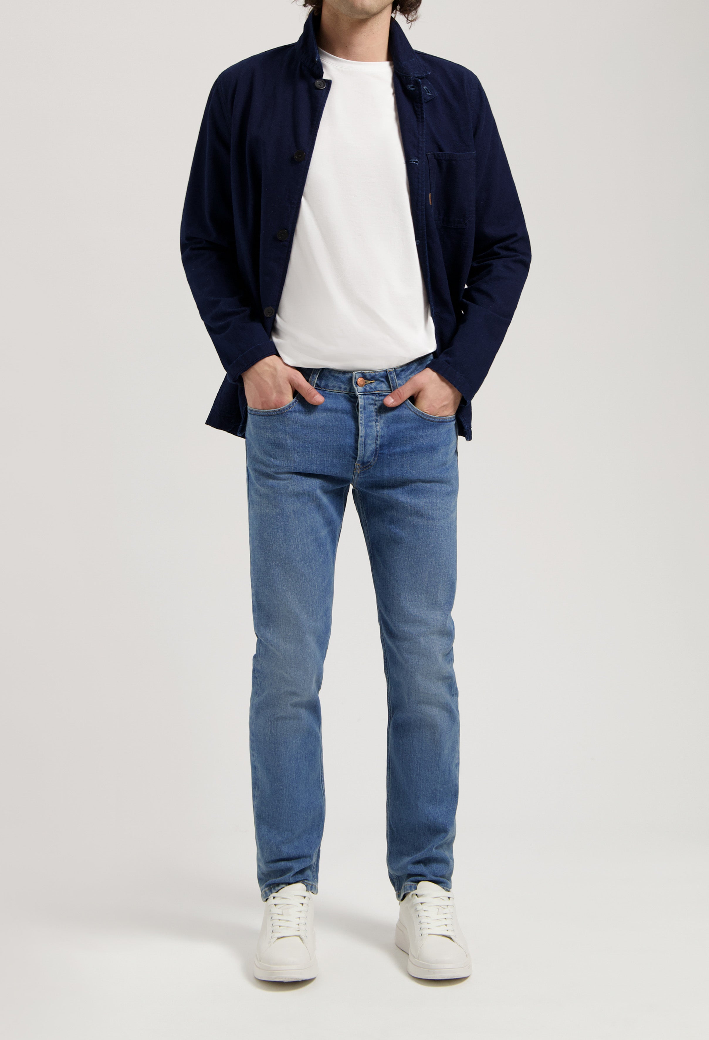 Sustainable MUD Jeans in light blue denim, crafted from organic cotton, paired with a white sweater for a classic look.