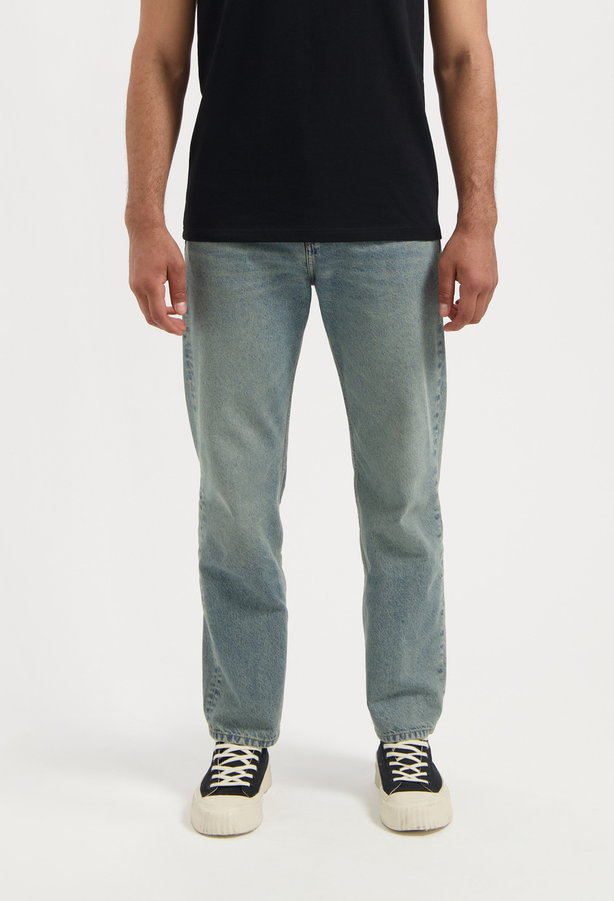 Man wearing sustainable MUD Jeans dark blue denim jacket over a tan shirt, emphasizing ethical fashion choices.