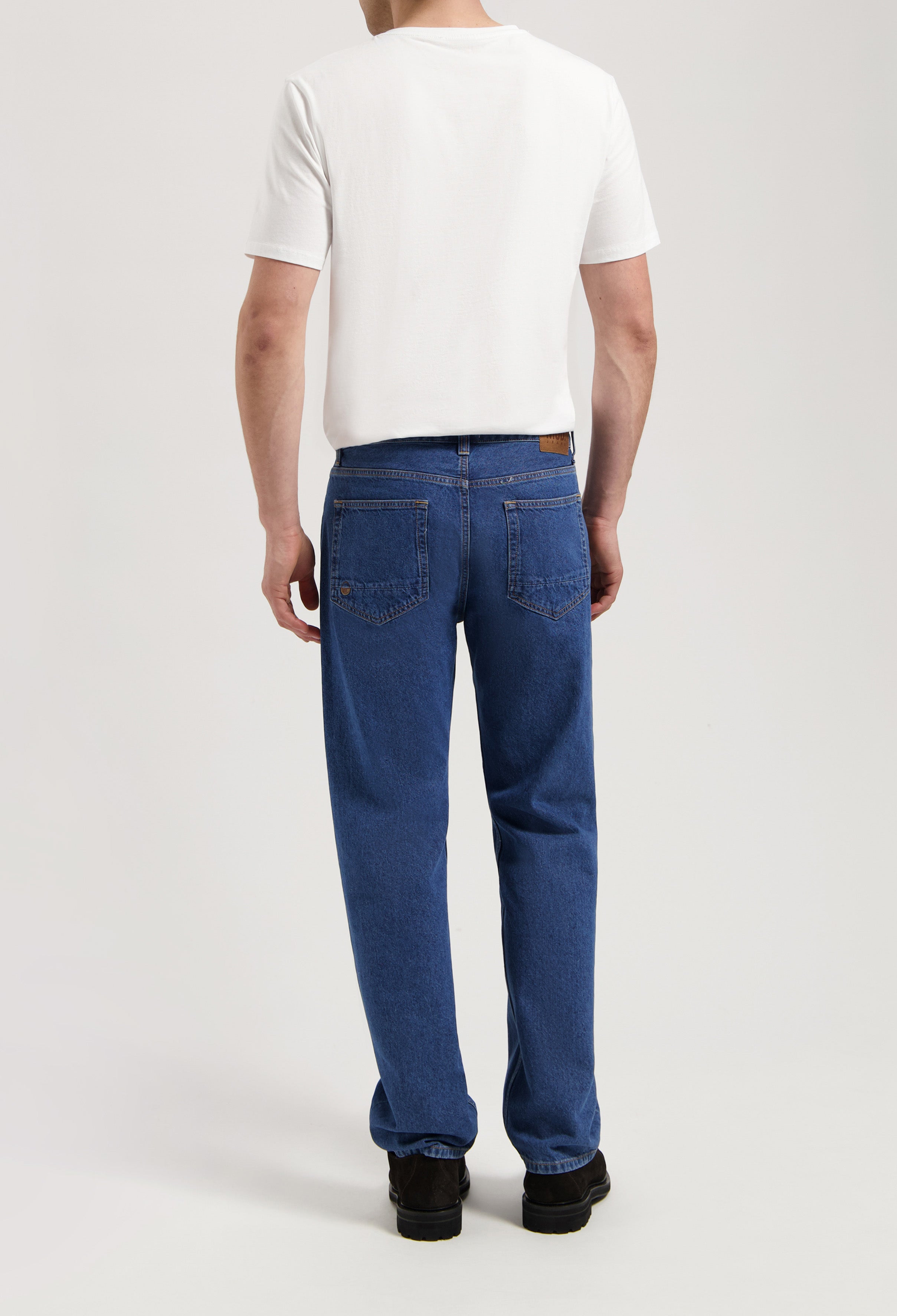 Sustainable MUD Jeans crafted from organic cotton, featuring dark gray denim and a comfortable fit, paired with a white tee.