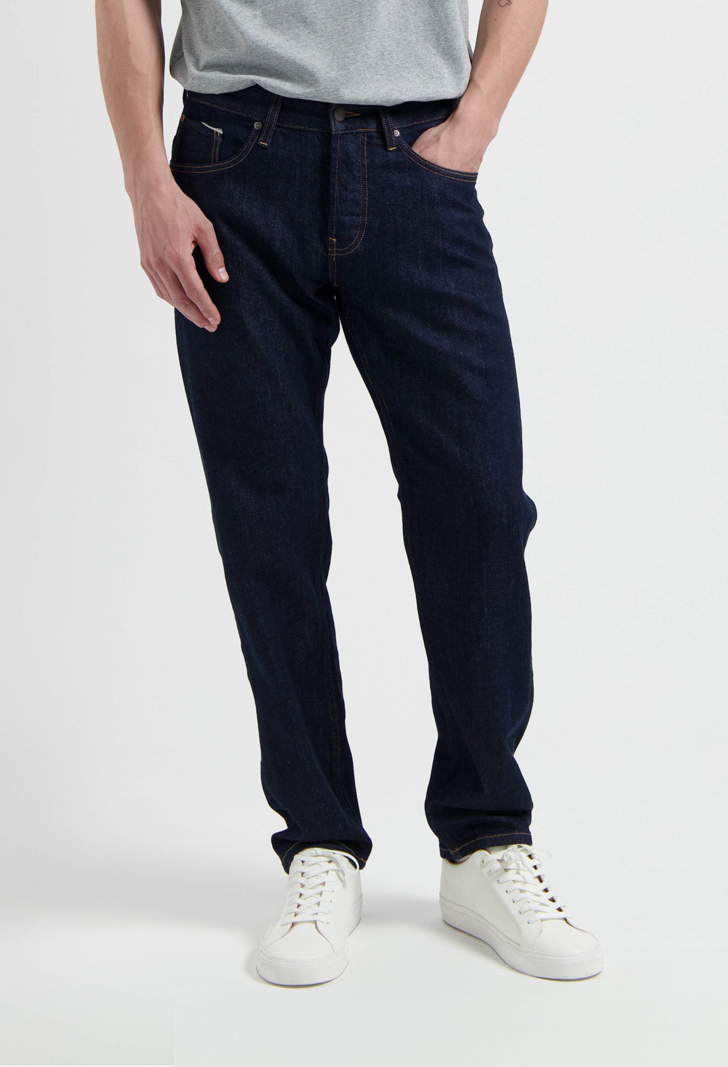 Sustainable MUD Jeans, classic fit in blue denim, crafted from organic cotton, paired with white sneakers and gray shirt.