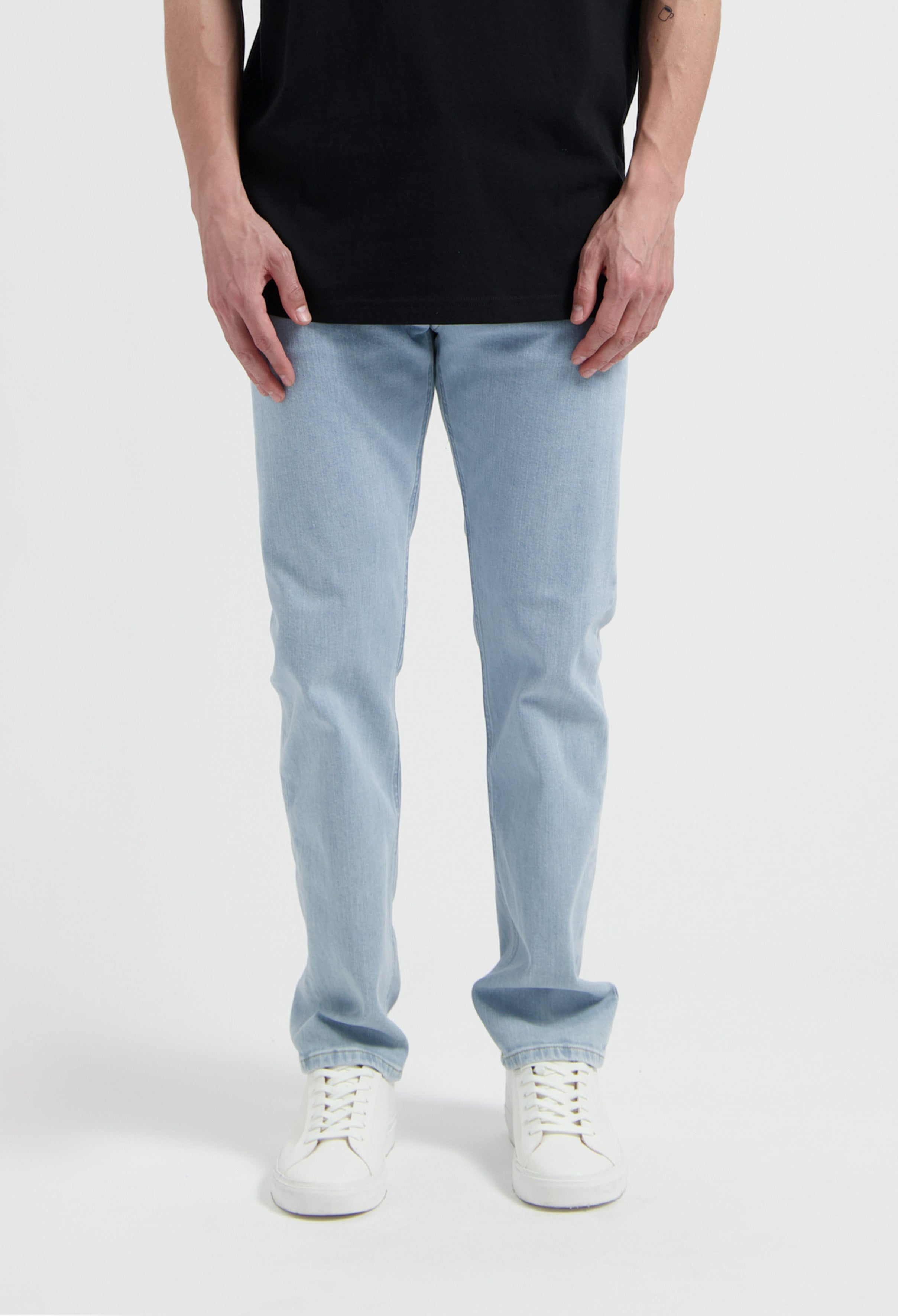 Sustainable MUD Jeans in light blue denim, crafted from organic cotton, worn with a cream sweater and black shoes.