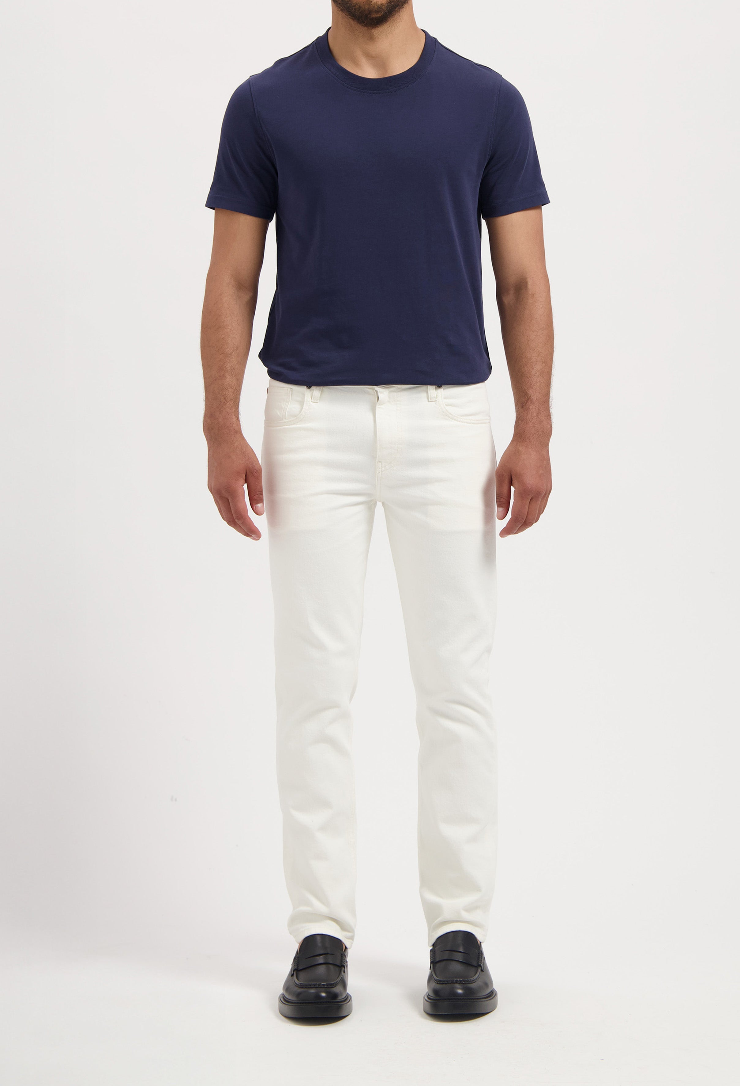 Sustainable MUD Jeans in a slim, white cotton design, paired with a navy t-shirt and black loafers for a classic look.