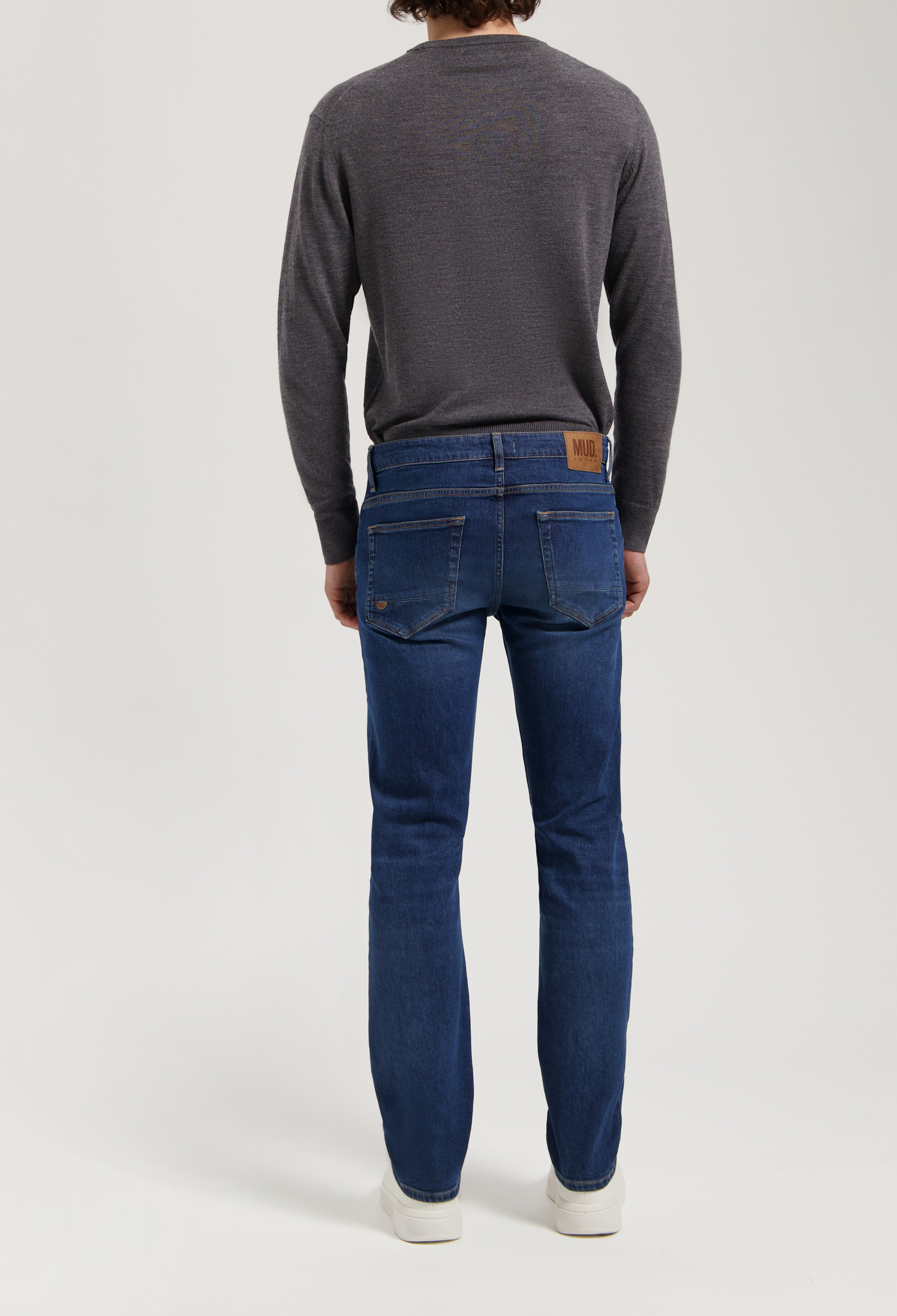Sustainable MUD Jeans in deep blue denim, classic straight fit, paired with a dark gray sweater, emphasizing ethical fashion.