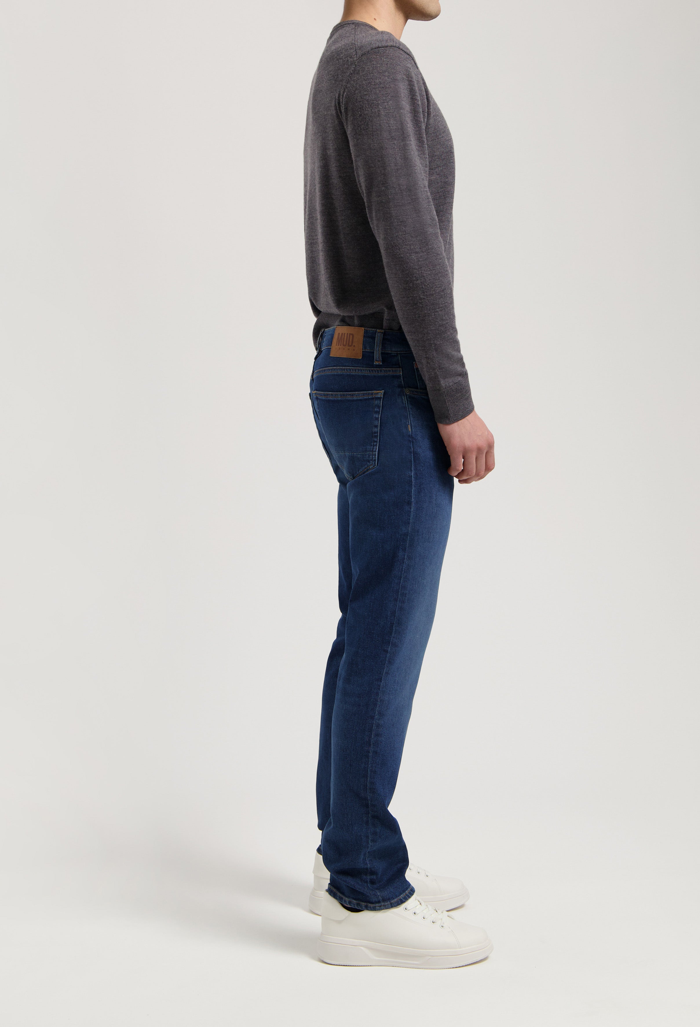 Sustainable MUD Jeans in dark blue denim, crafted ethically with organic cotton, paired with a gray sweater.