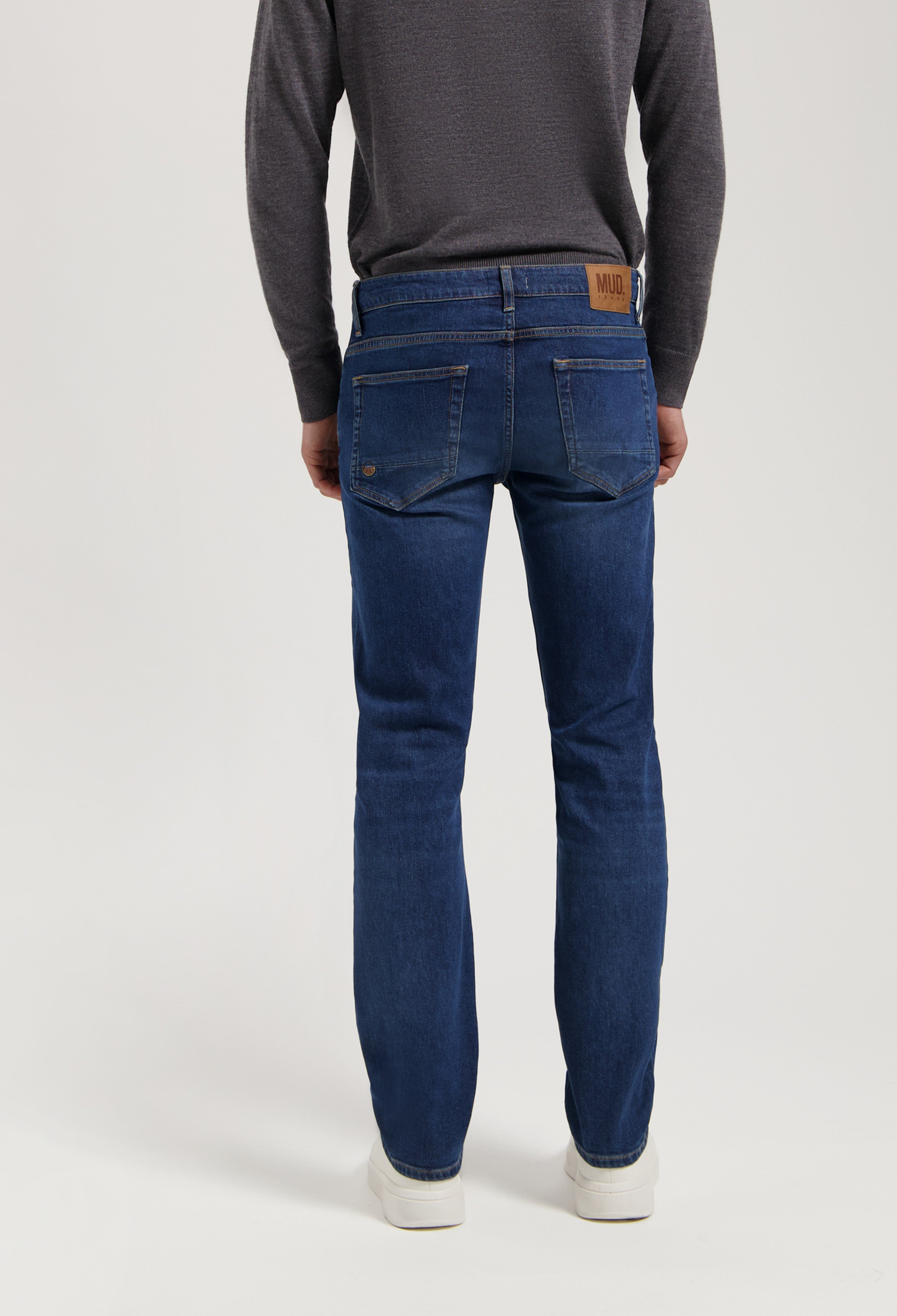 Sustainable MUD Jeans in dark blue denim, crafted for ethical style, paired with a gray sweater, shown from the back.