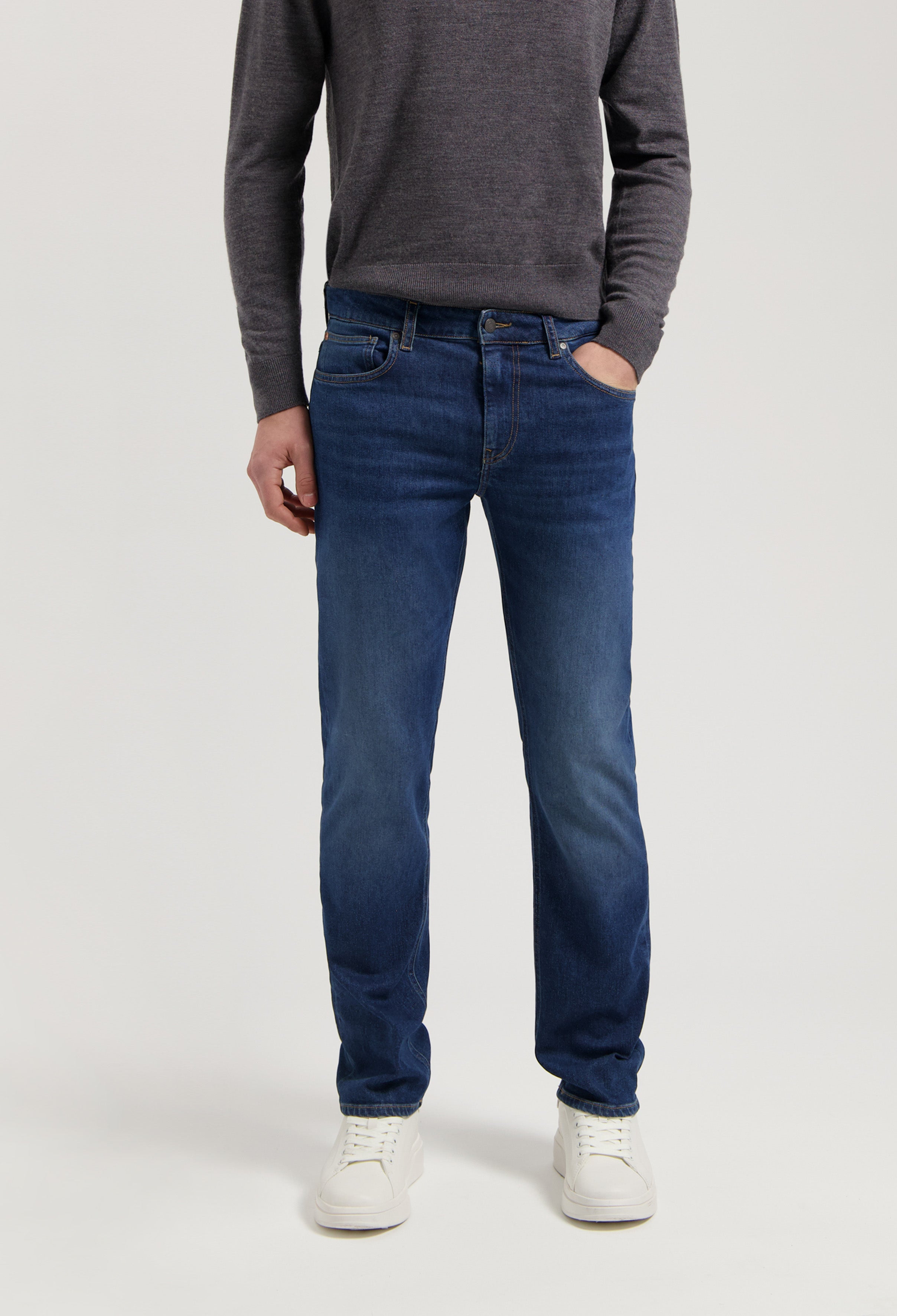Sustainable MUD Jeans, ethical dark blue denim in a regular fit, paired with a charcoal gray sweater.