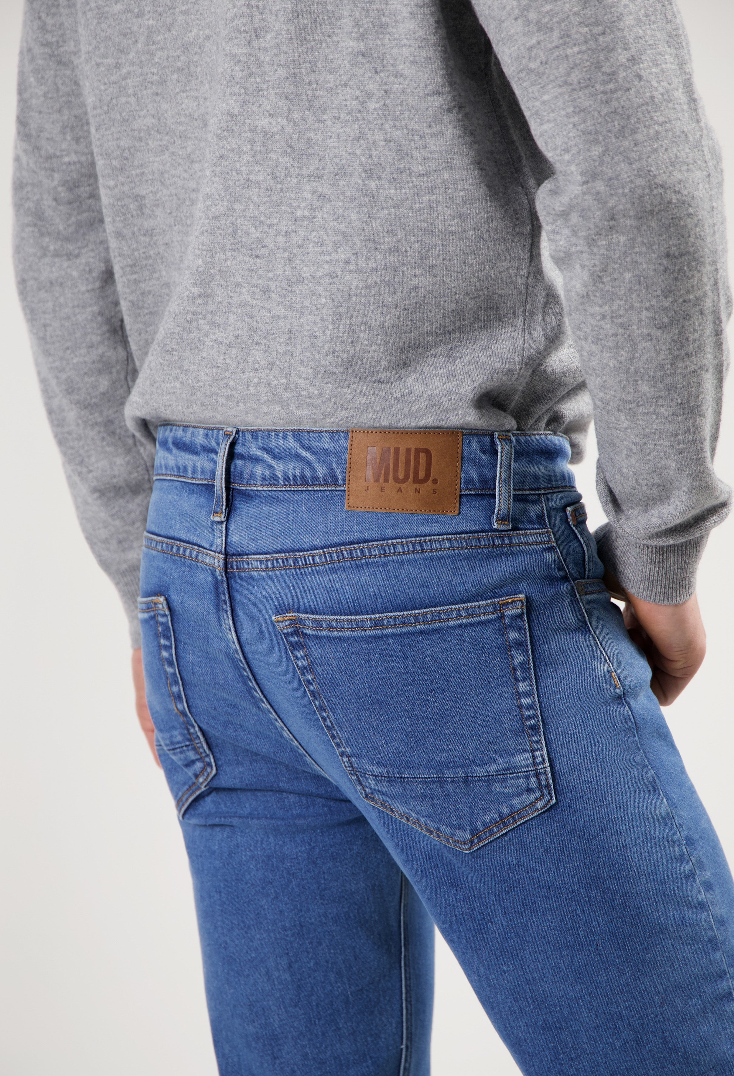 Sustainable MUD Jeans in classic blue denim, crafted from organic cotton, paired with a cozy gray sweater for ethical style.
