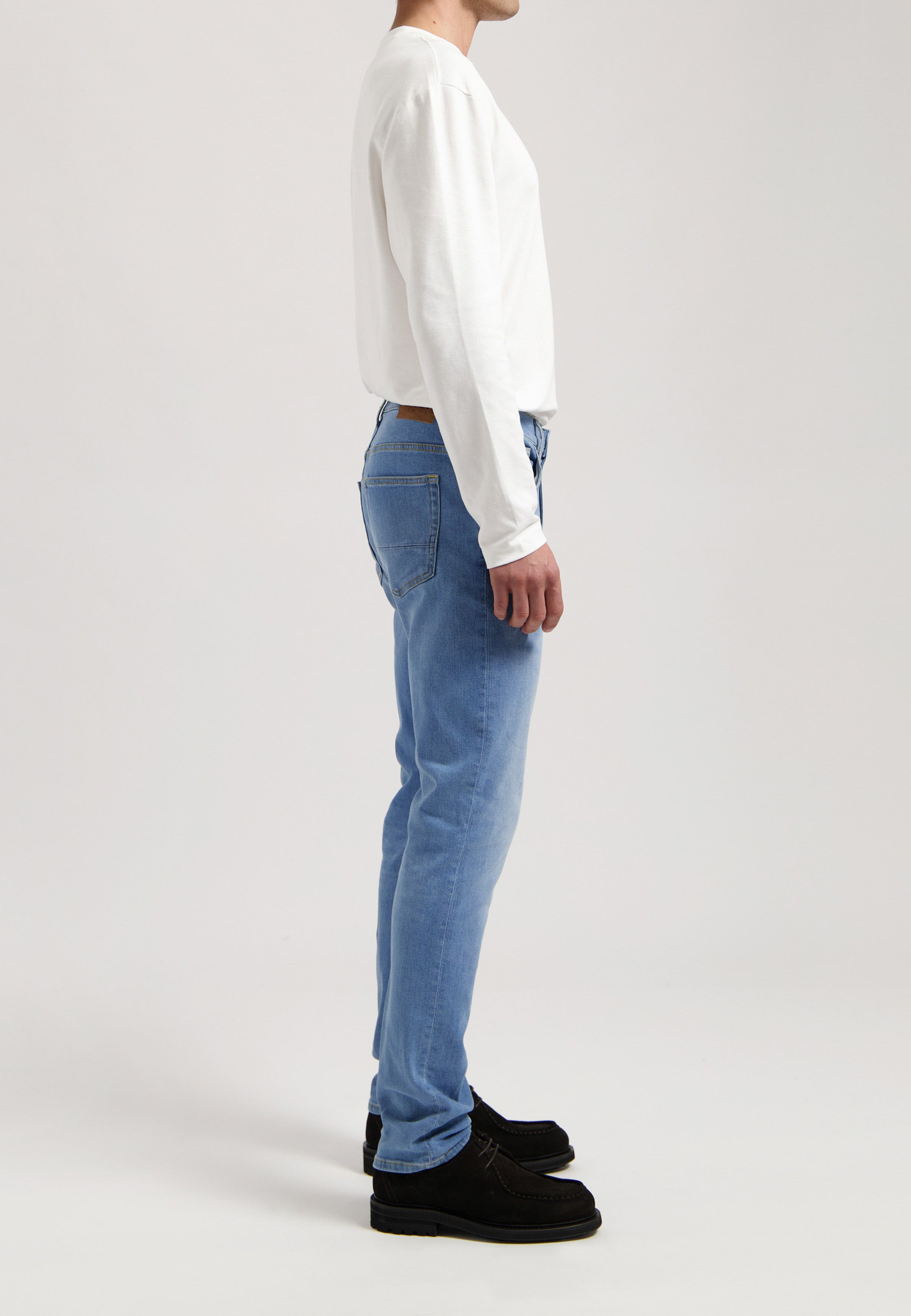 Sustainable MUD Jeans in deep blue denim, crafted ethically from organic cotton, paired with a gray sweater.