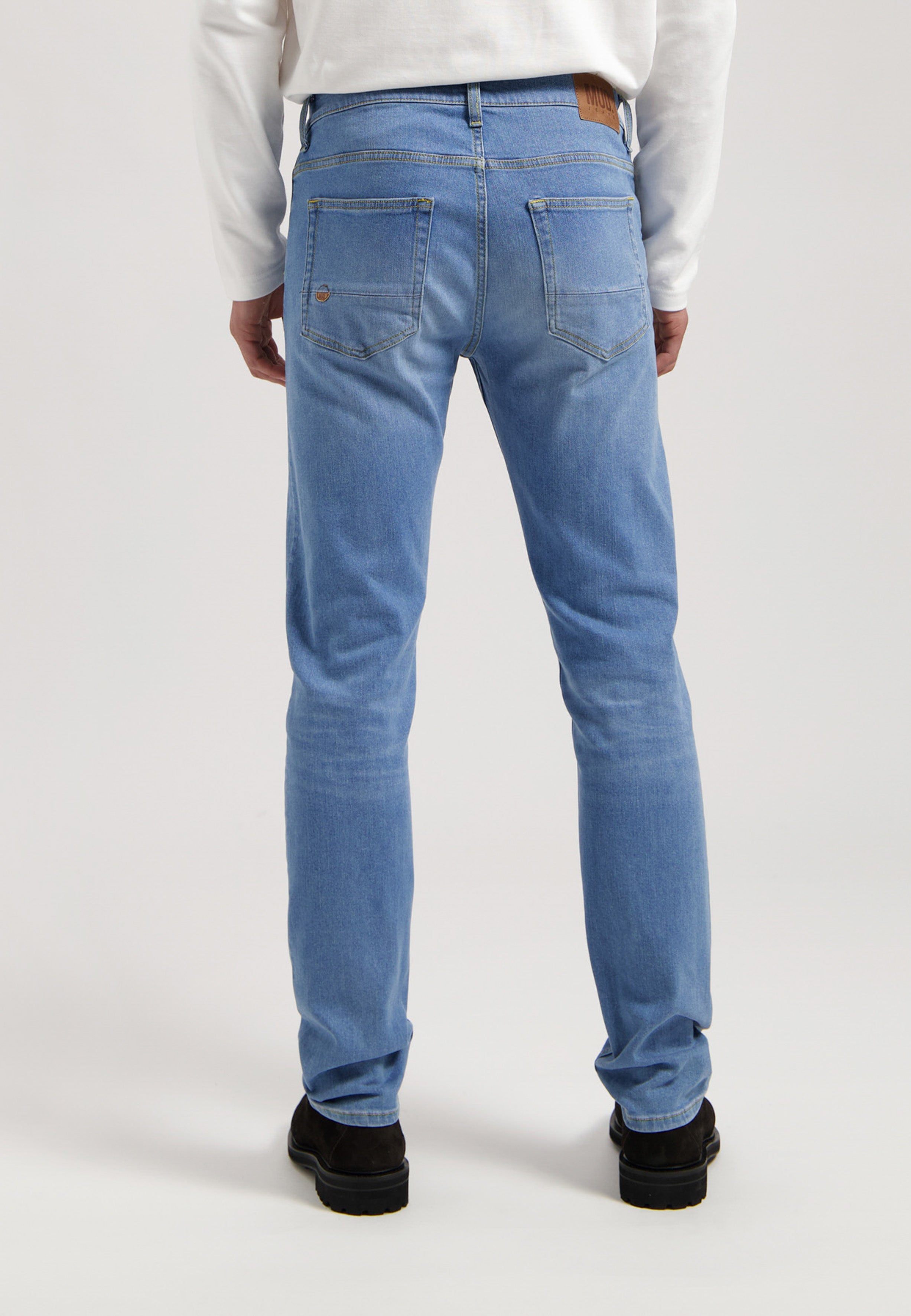 Sustainable Mud Jeans in light blue denim, crafted ethically, paired with a gray T-shirt and white sneakers.