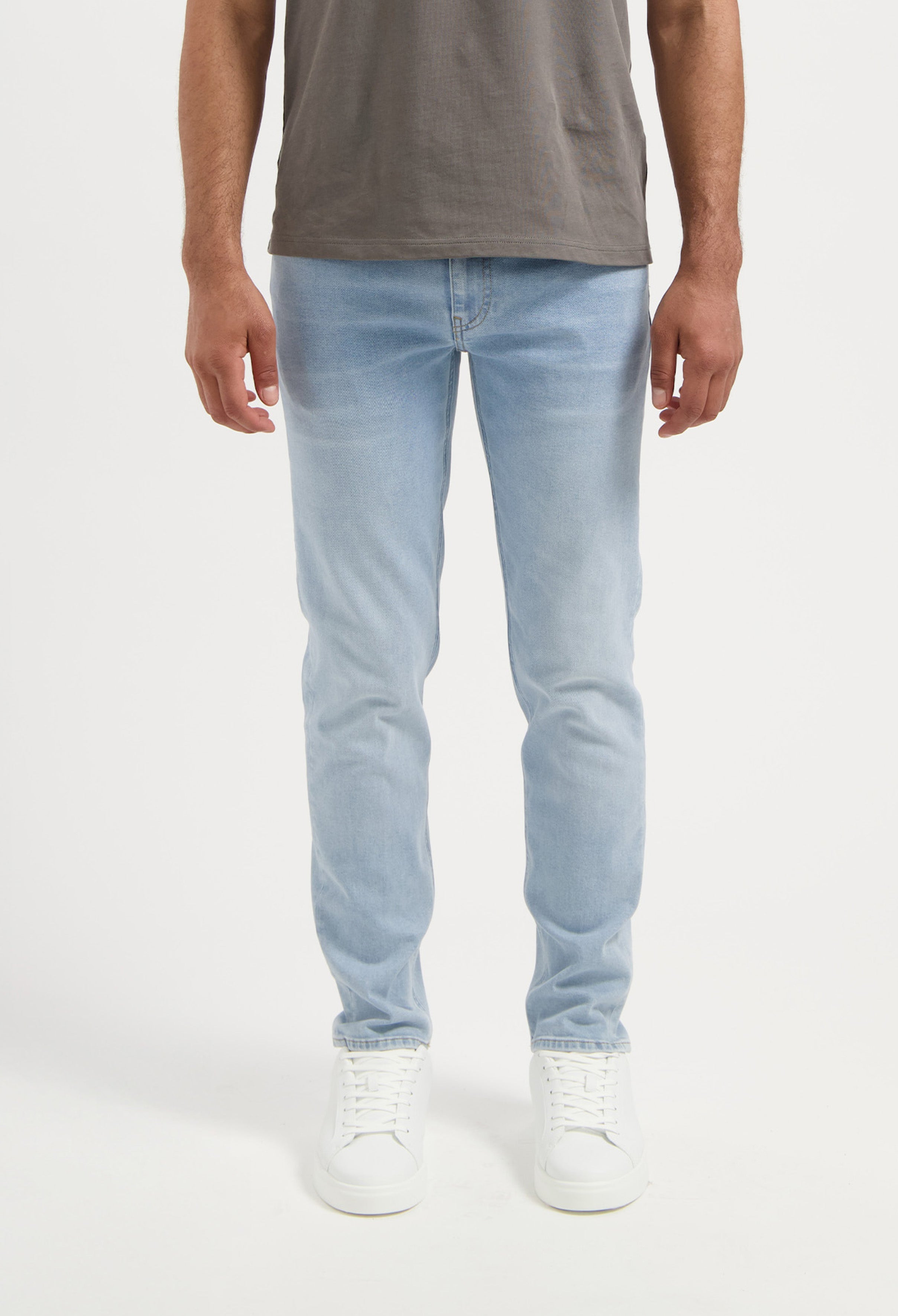 Sustainable MUD Jeans in beige, designed with ethical materials, paired with a gray t-shirt and white sneakers.