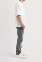 Sustainable MUD Jeans in gray denim, featuring a slim fit, paired with a black turtleneck and white sneakers.