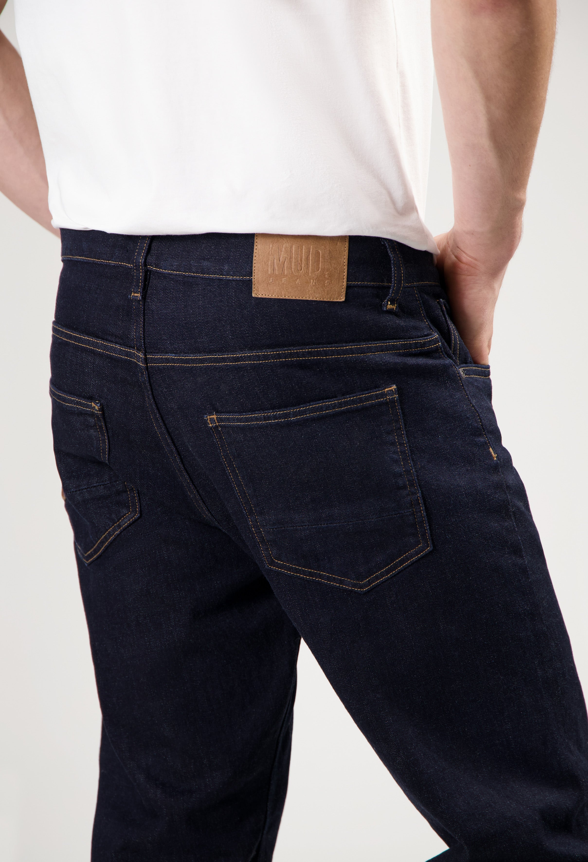 Sustainable MUD Jeans in deep blue denim, crafted from organic cotton, paired with a charcoal gray long-sleeve top.