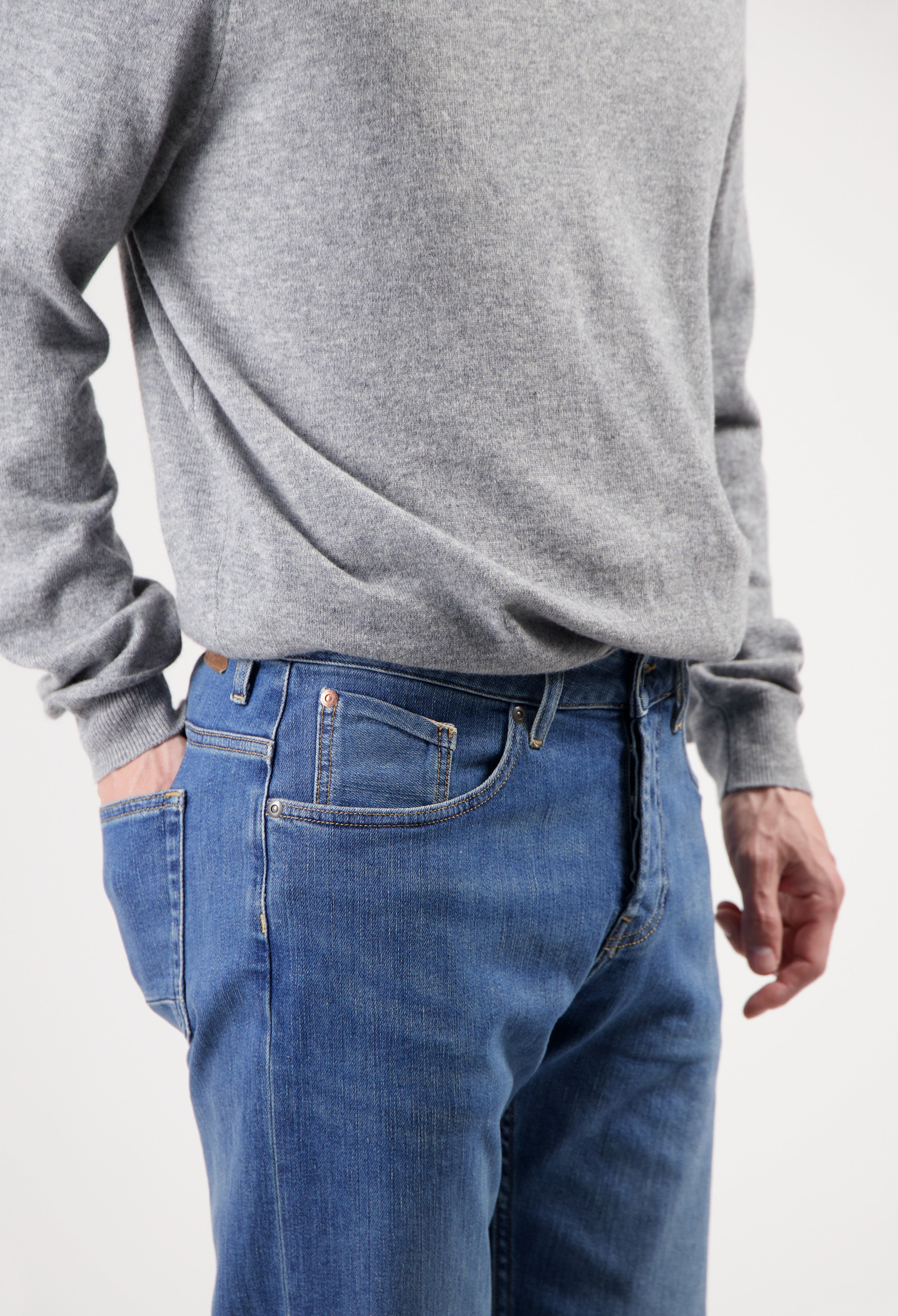 Sustainable MUD Jeans in deep blue denim, crafted from organic cotton, paired with a soft gray sweater.