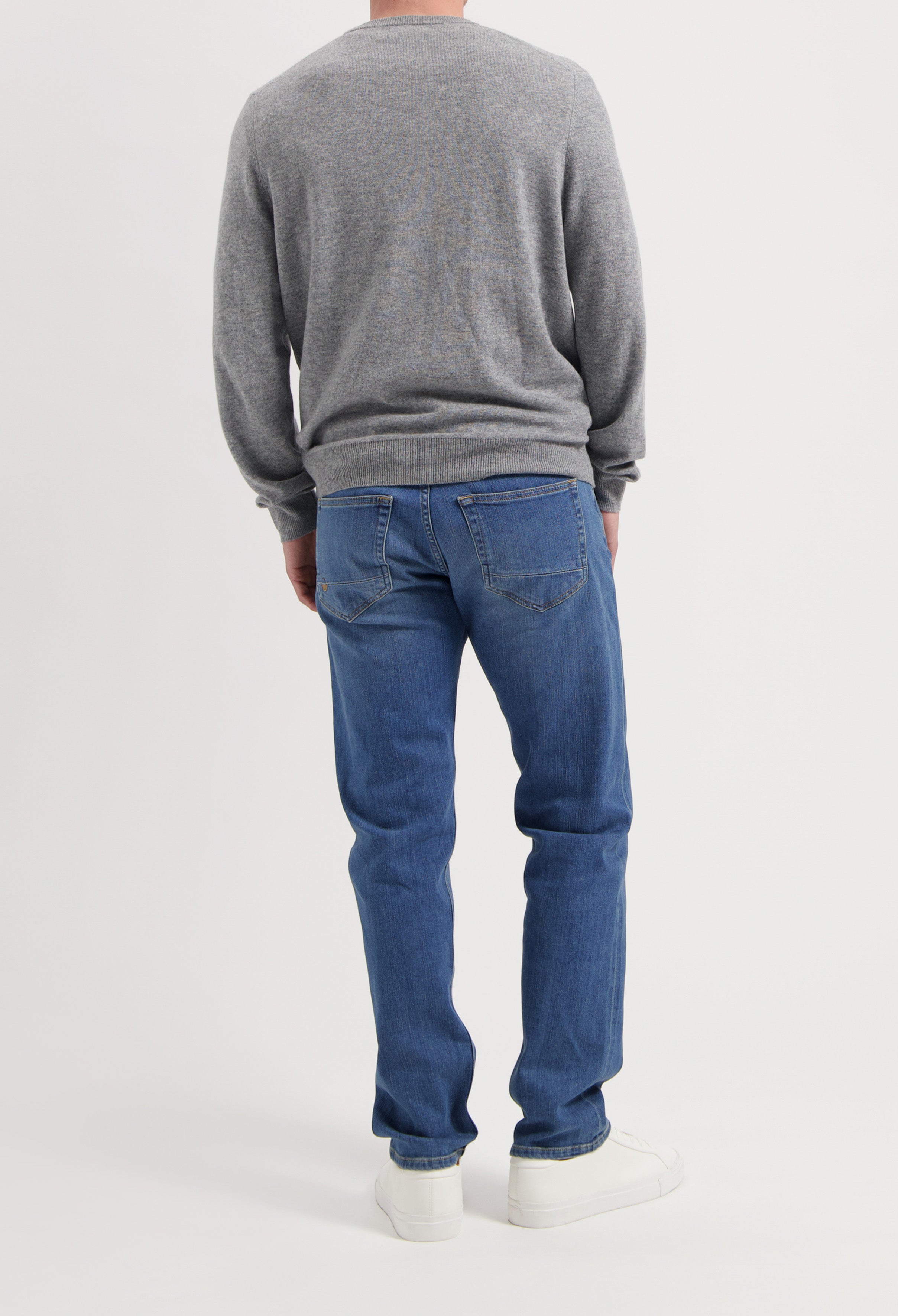 Sustainable MUD Jeans in blue denim, paired with a navy shirt and white sneakers, embodying ethical fashion.