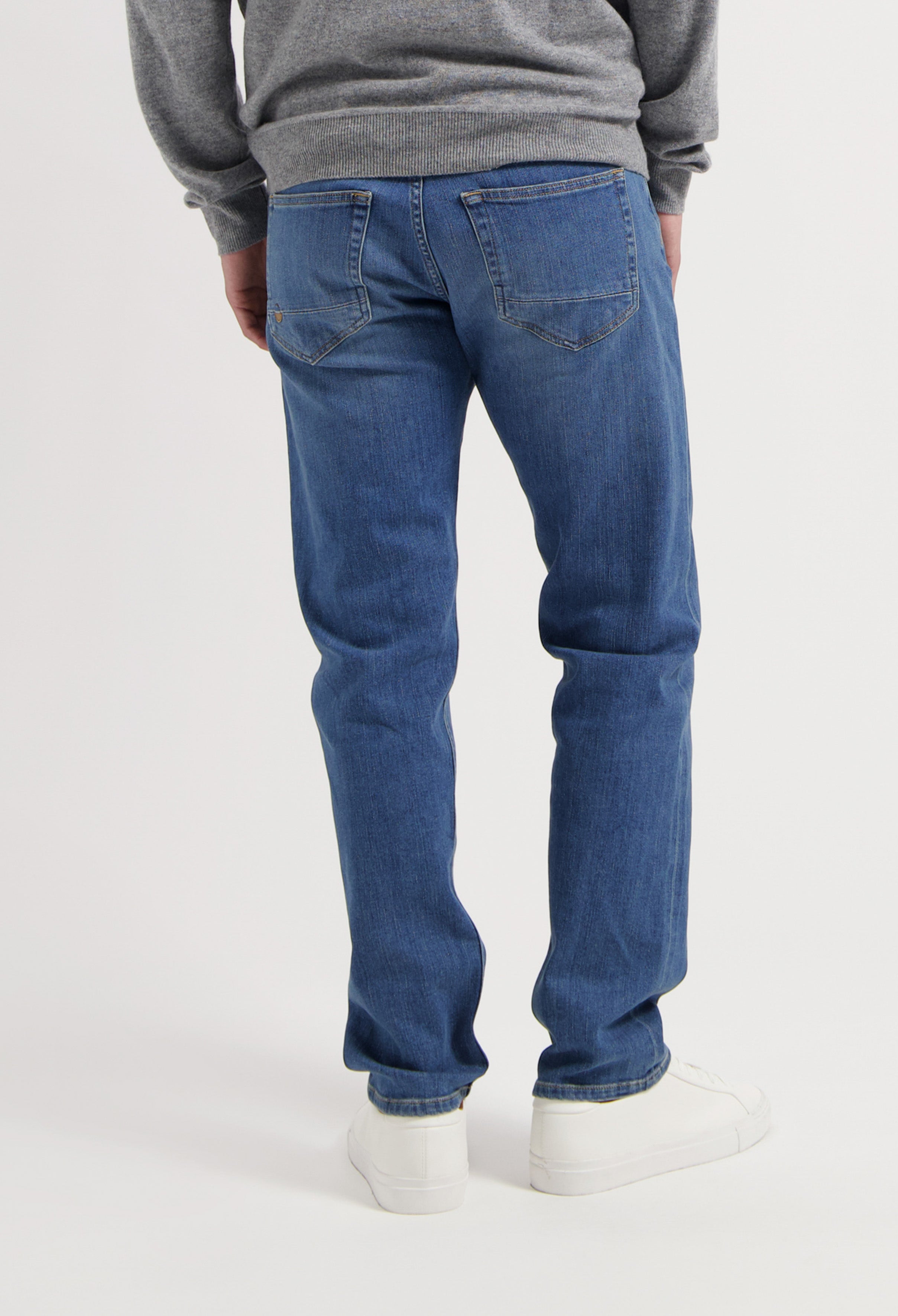 Sustainable MUD Jeans featuring dark blue denim, styled with a gray sweater and white sneakers for an ethical look.