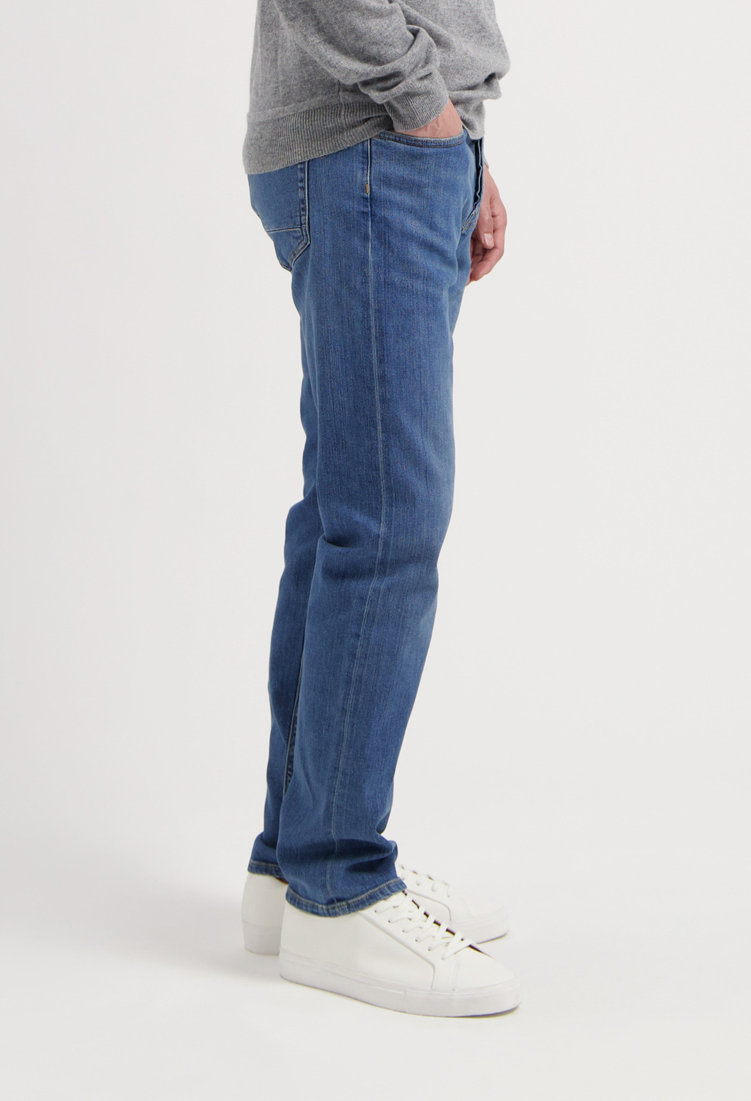 Sustainable MUD Jeans in dark blue denim, crafted from organic cotton, worn with a gray sweater and white sneakers.