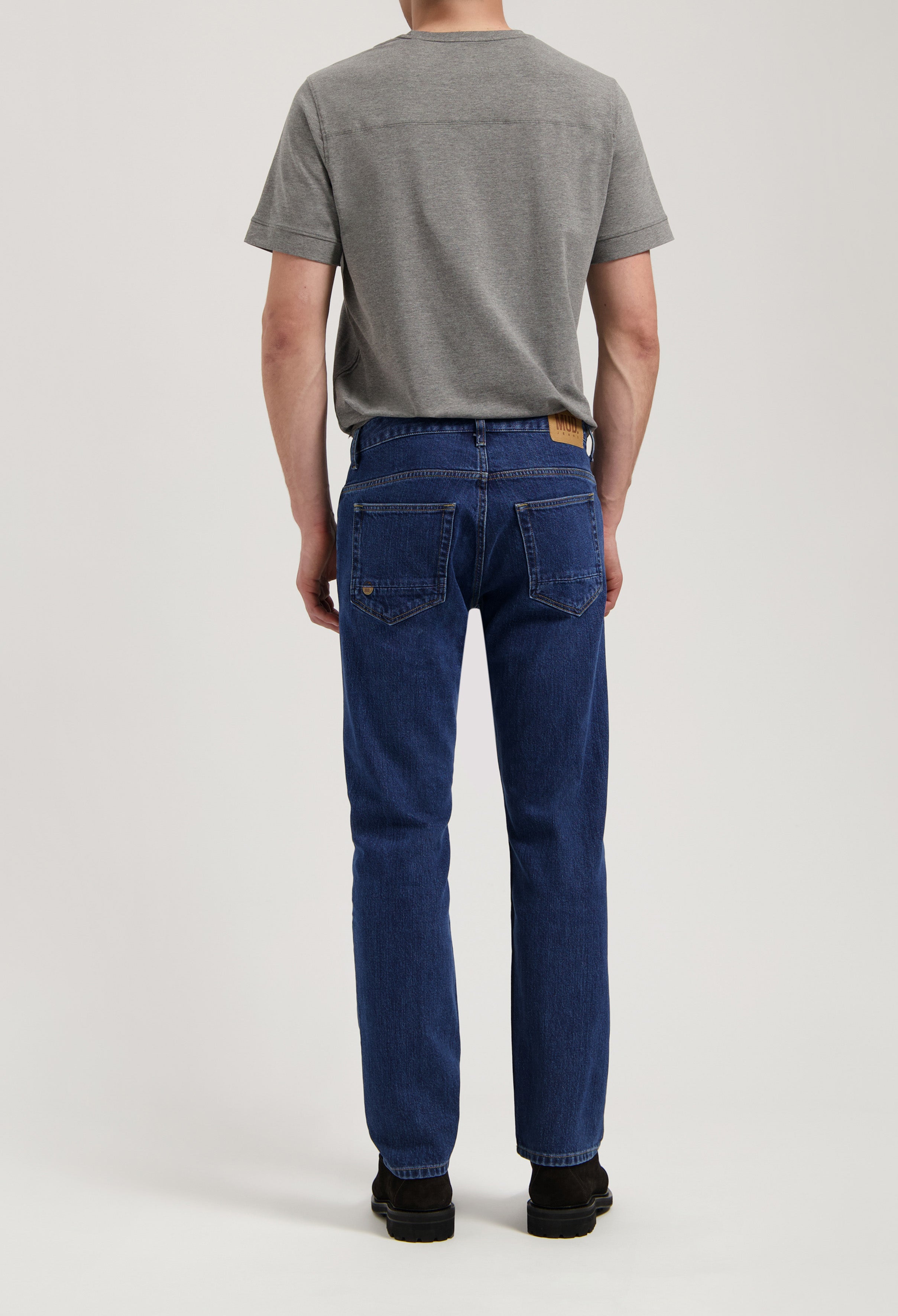 Model wearing Hank Mid Tapered jeans in medium stone, made from sustainable organic and recycled cotton, offering a tapered fit.