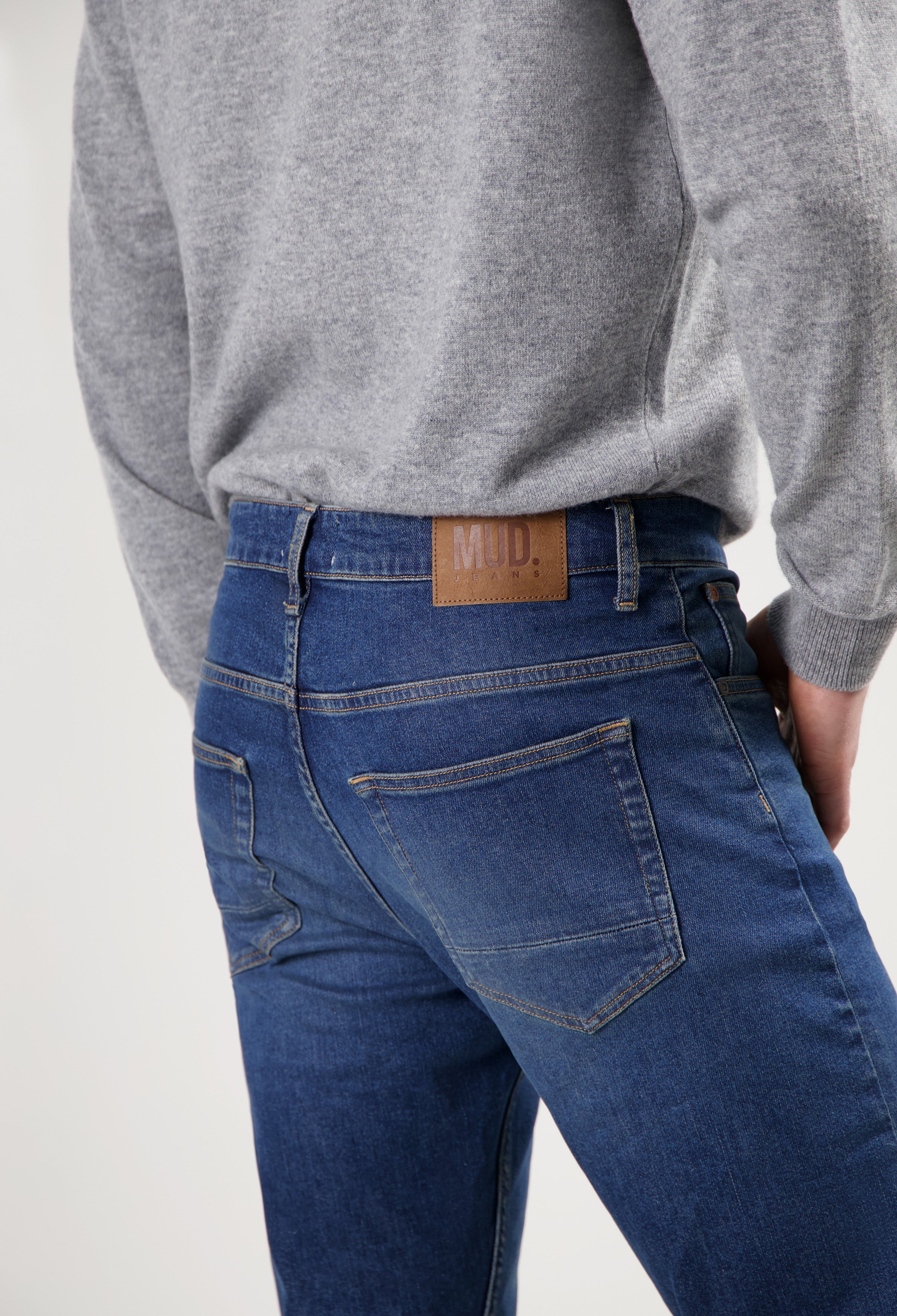 Sustainable MUD Jeans made from organic cotton, featuring deep blue denim in a modern fit, paired with a gray sweater.