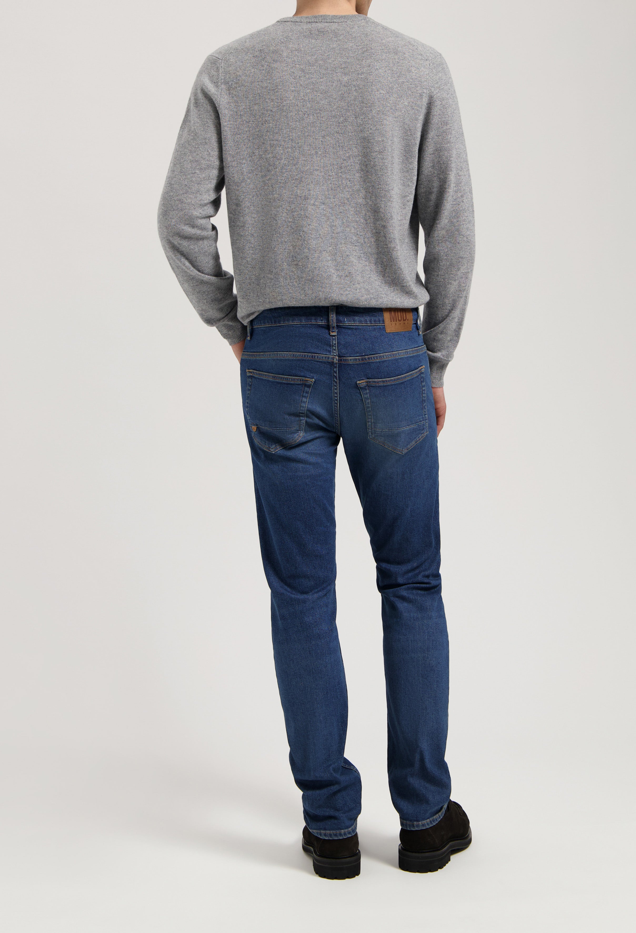 Sustainable MUD Jeans in a medium blue denim, made from organic cotton, paired with a gray sweater, showcasing ethical fashion.