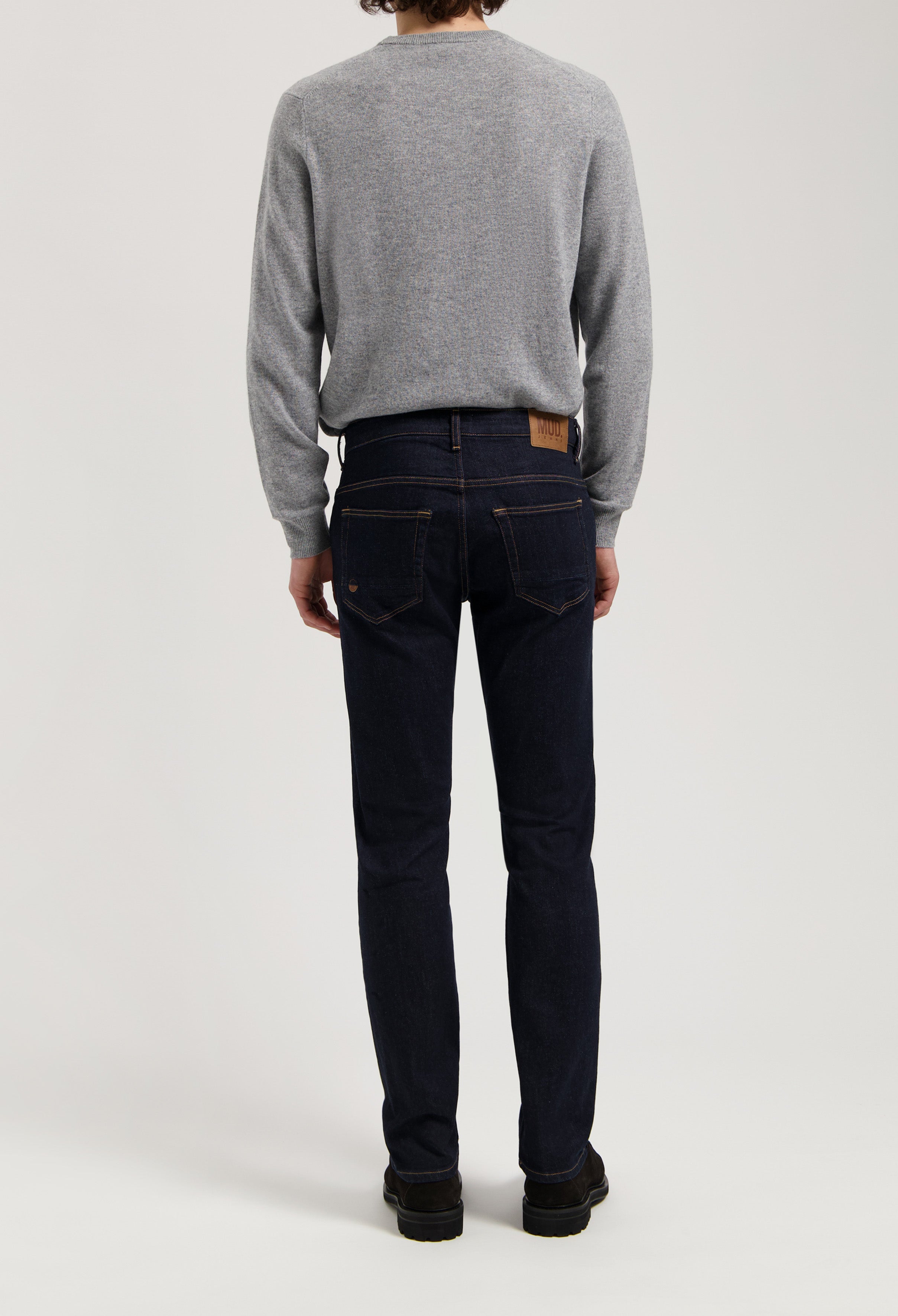 Sustainable MUD Jeans in dark denim, crafted ethically, paired with a gray sweater for a classic, eco-friendly style.