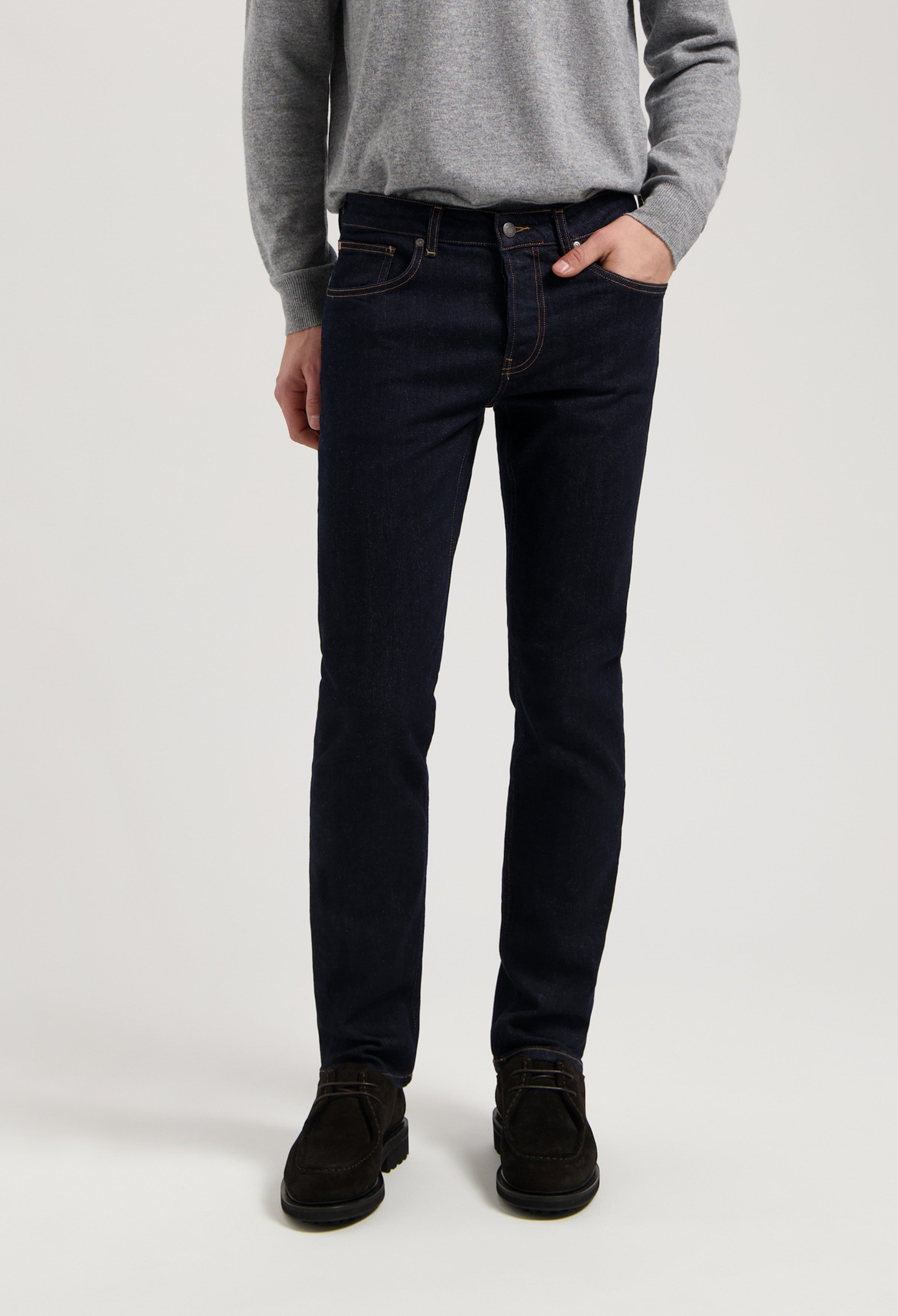 Sustainable MUD Jeans in dark blue organic cotton, featuring a slim fit design, paired with a cozy gray sweater.