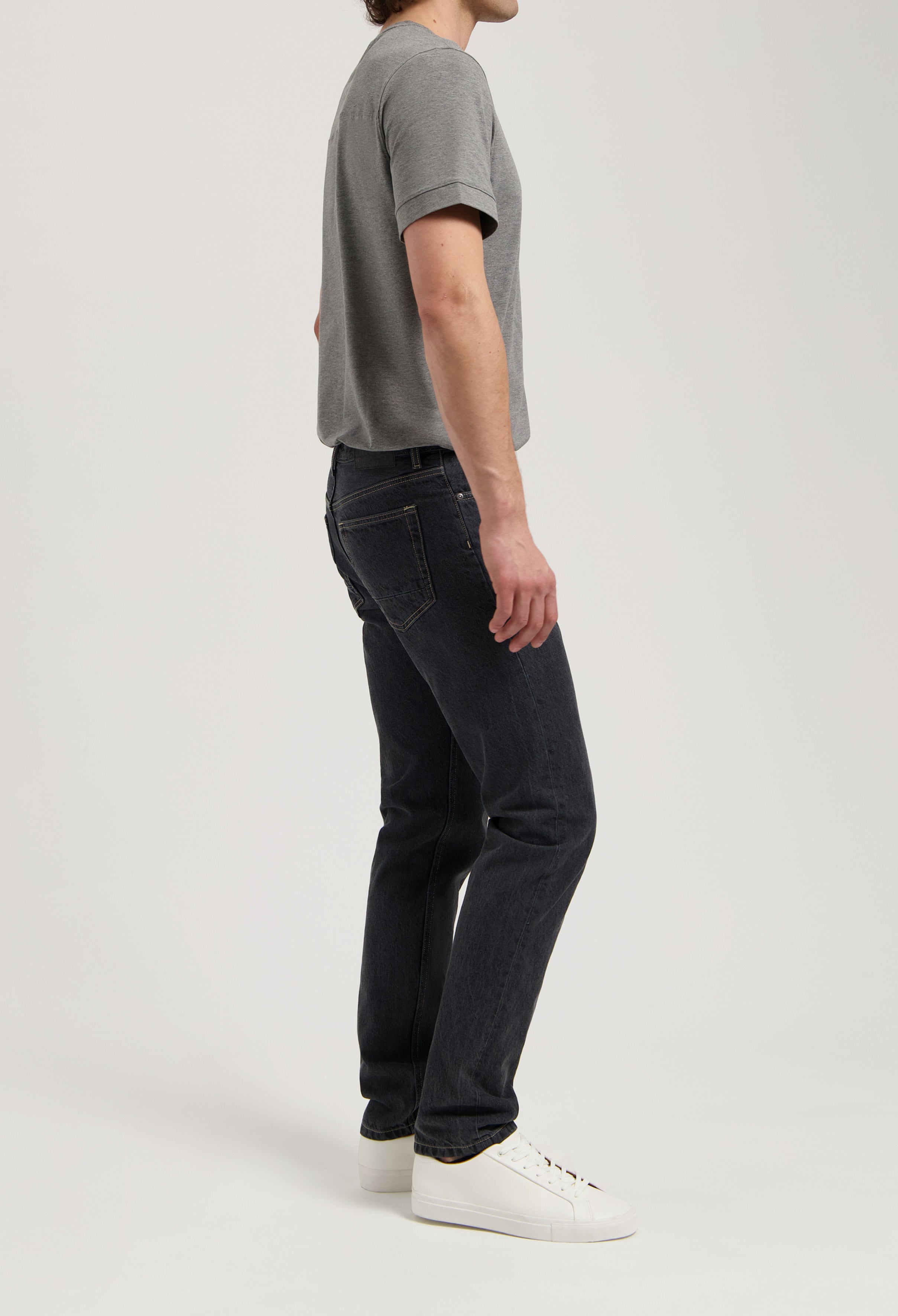 Sustainable MUD Jeans in dark denim, crafted ethically, worn with a cream knit sweater and black shoes.