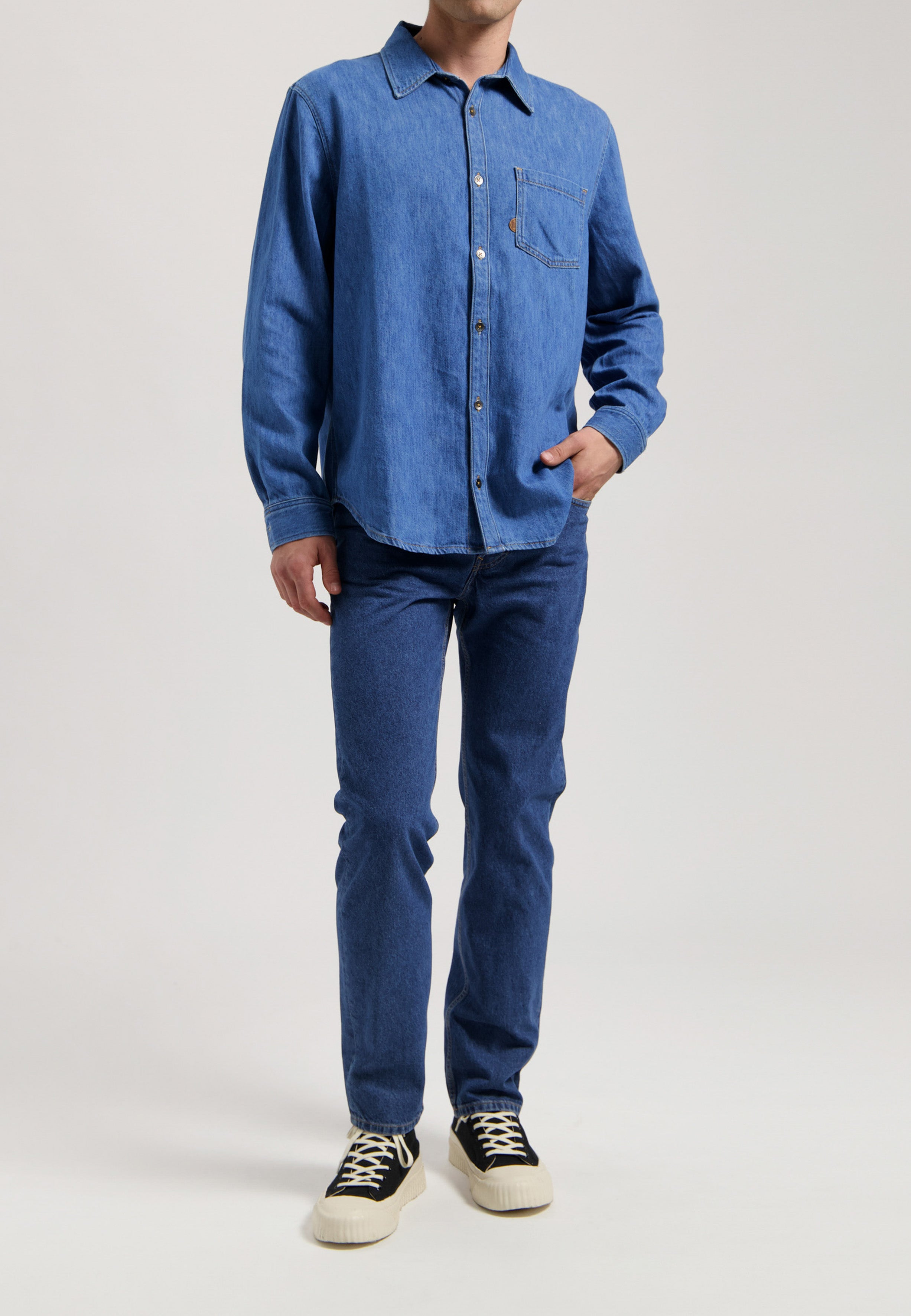 Sustainable MUD Jeans in deep indigo, made from organic cotton, paired with a simple white long-sleeved shirt.
