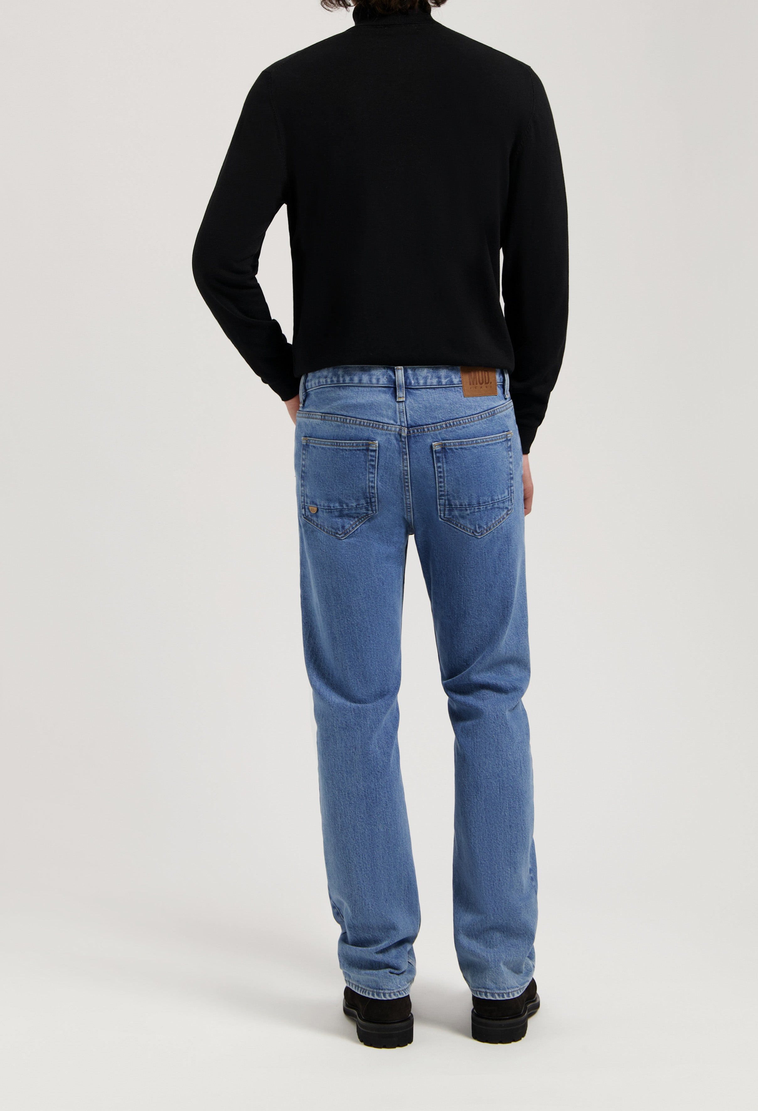 Sustainable MUD Jeans in classic blue denim, crafted from ethical materials, paired with a sleek black sweater.