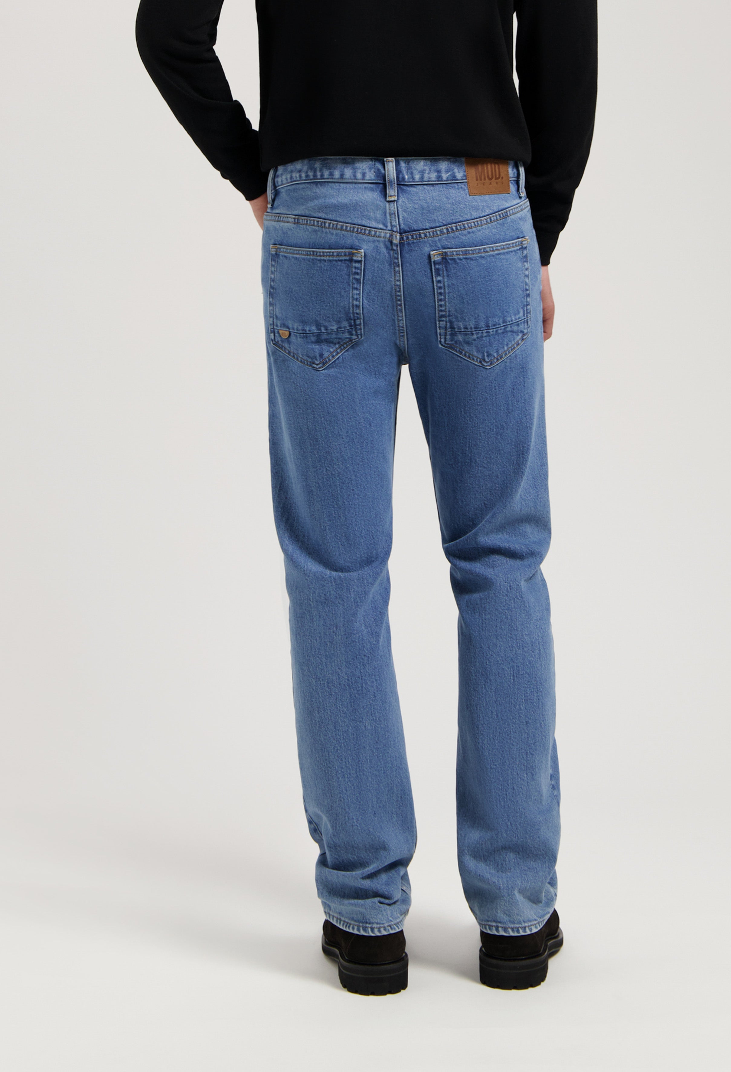 Sustainable MUD Jeans in light blue denim, featuring a classic fit with ethical craftsmanship, paired with black shoes.