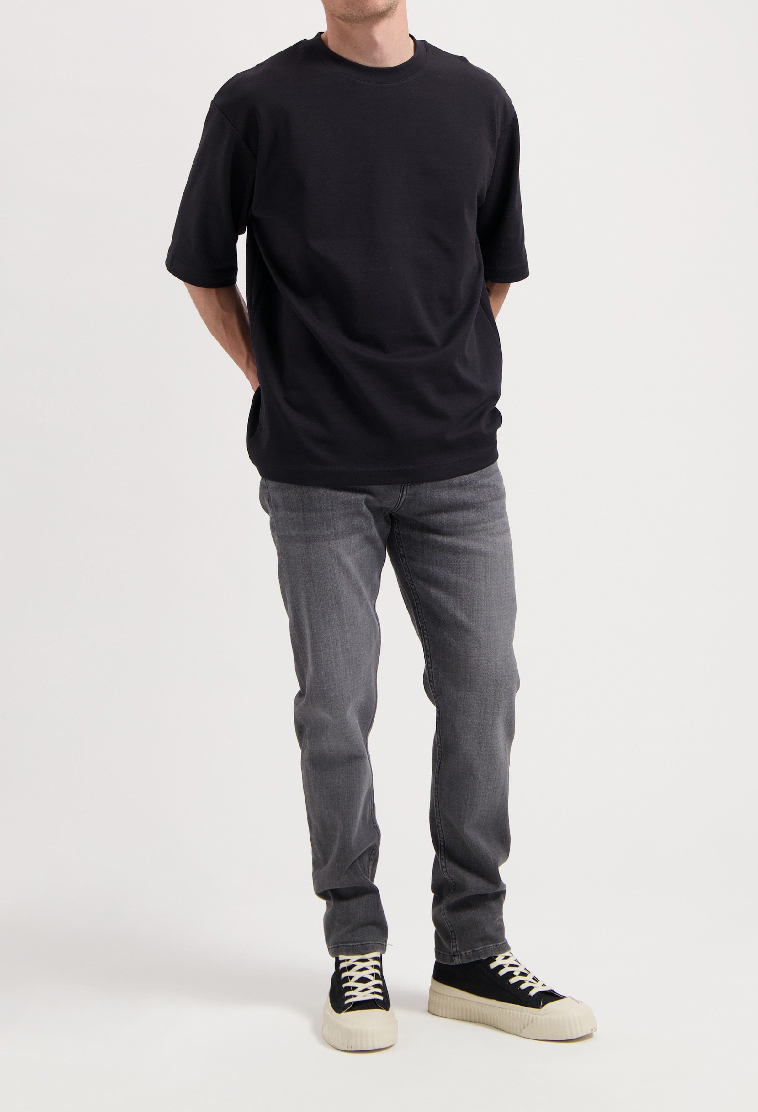 Sustainable MUD Jeans in dark blue denim, crafted from organic cotton, worn with a gray tee and white sneakers.