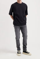 Sustainable MUD Jeans in dark blue denim, crafted from organic cotton, worn with a gray tee and white sneakers.