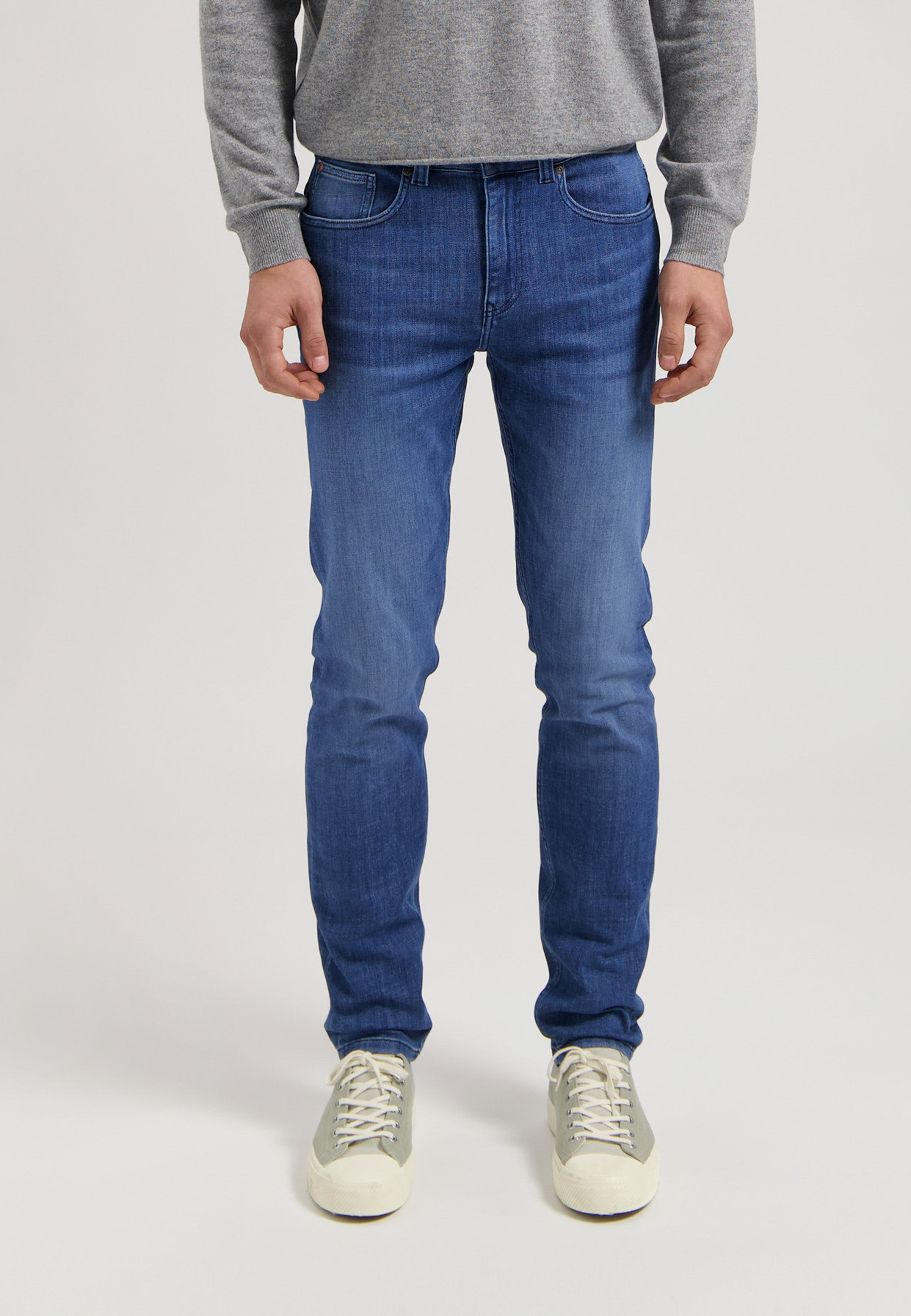 Sustainable MUD Jeans in a deep blue denim, ethically made, paired with a cozy gray sweater and white sneakers.