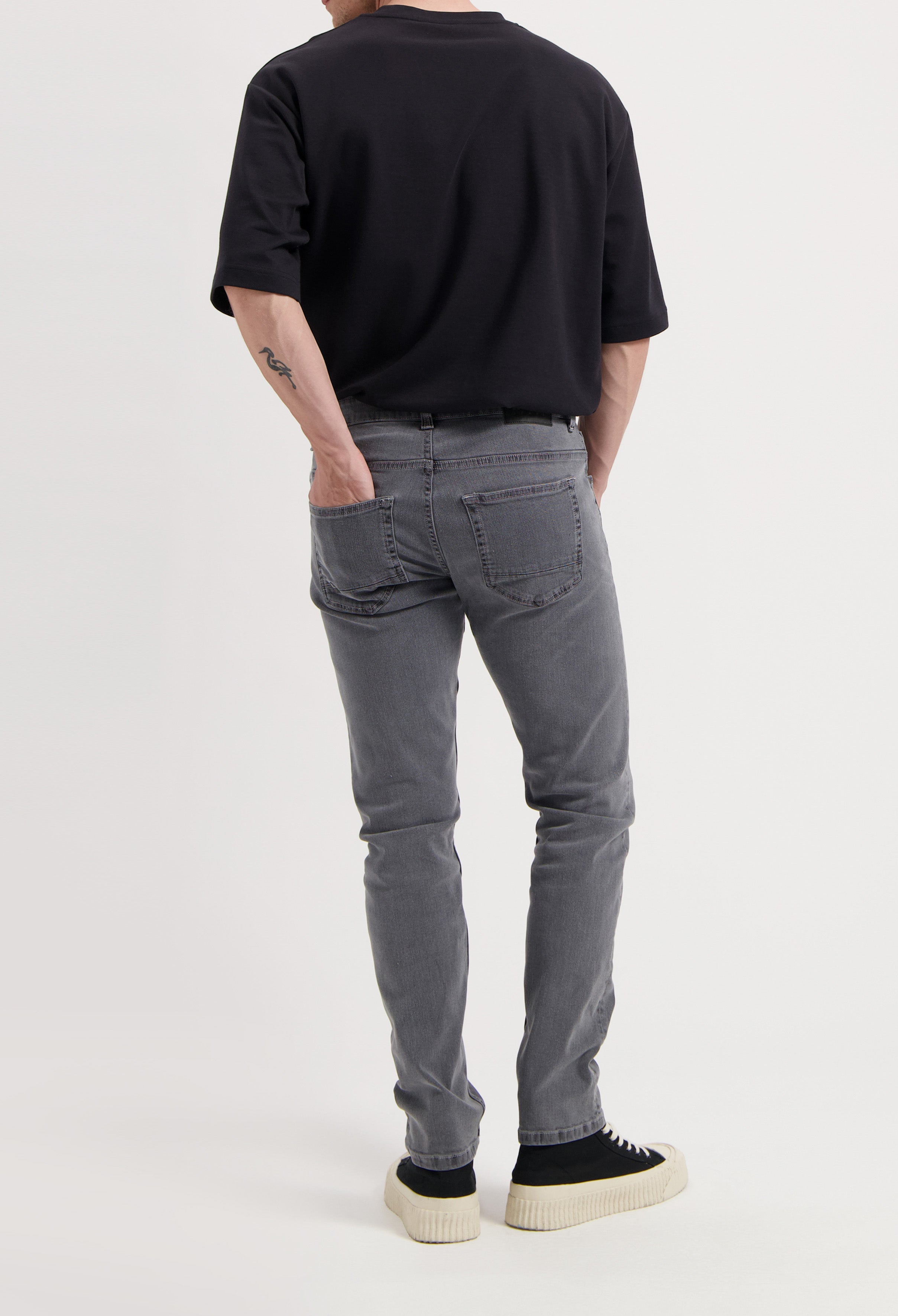 Sustainable MUD Jeans in light blue, slim fit, crafted from organic cotton, paired with white sneakers and a shirt.