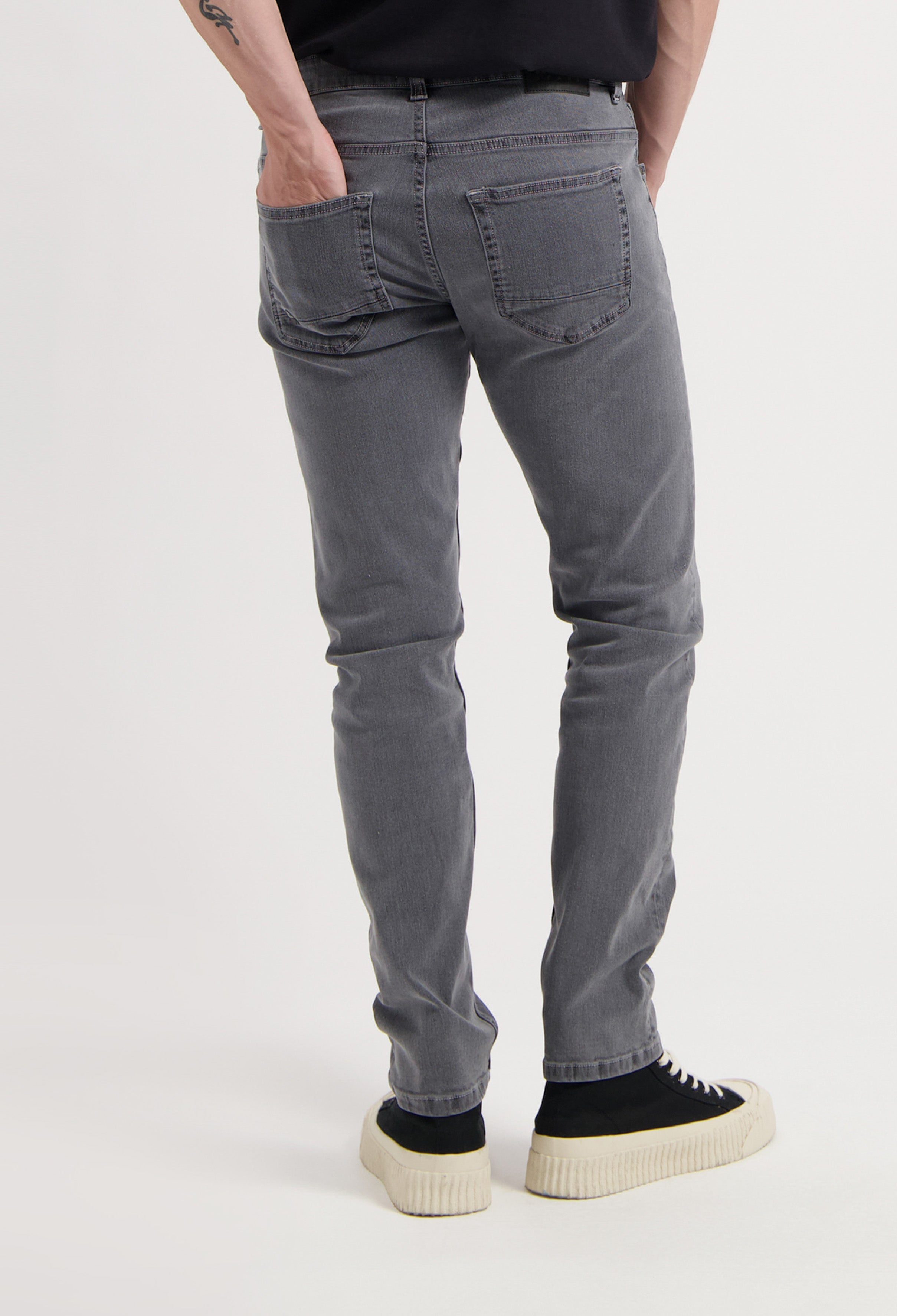 Sustainable MUD Jeans in dark gray denim, ethically made with organic cotton, paired with a white long-sleeve top.