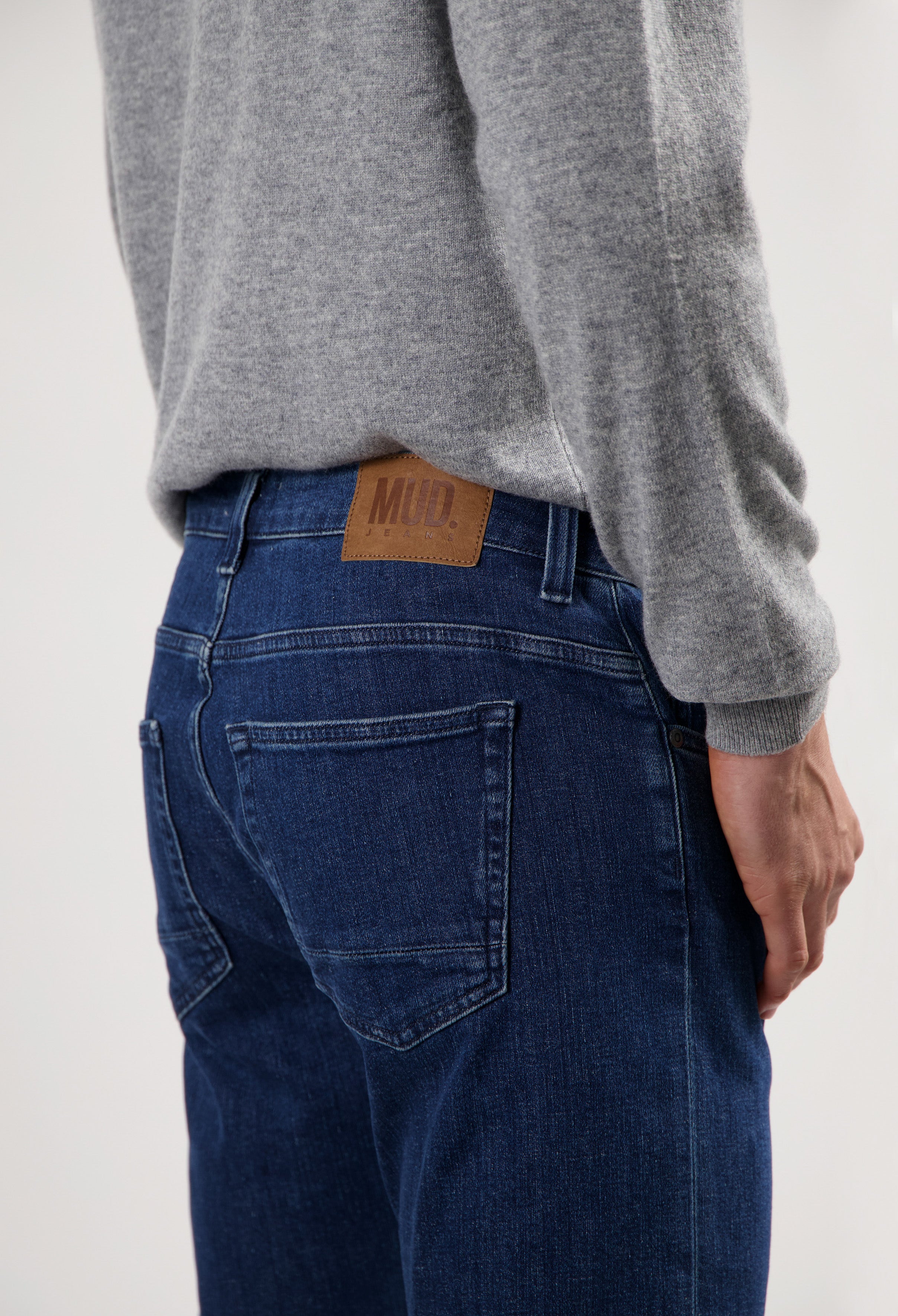 Sustainable MUD Jeans made from organic cotton in classic blue, paired with a light gray sweater and white sneakers.